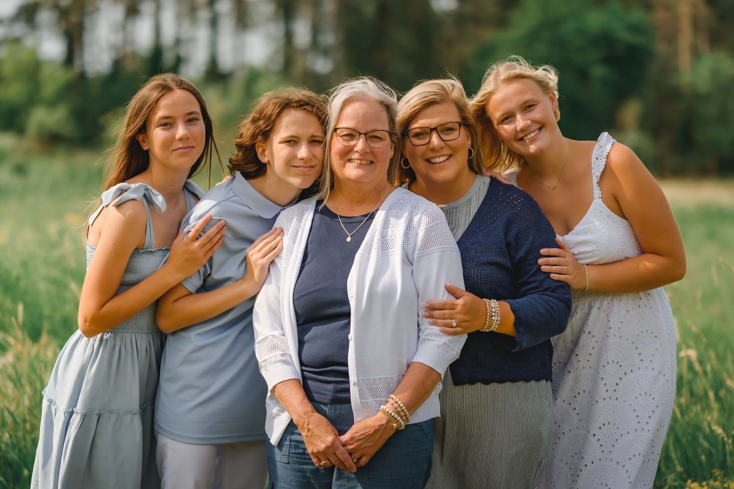 Five women smiling together outdoors in a green summer meadow setting.