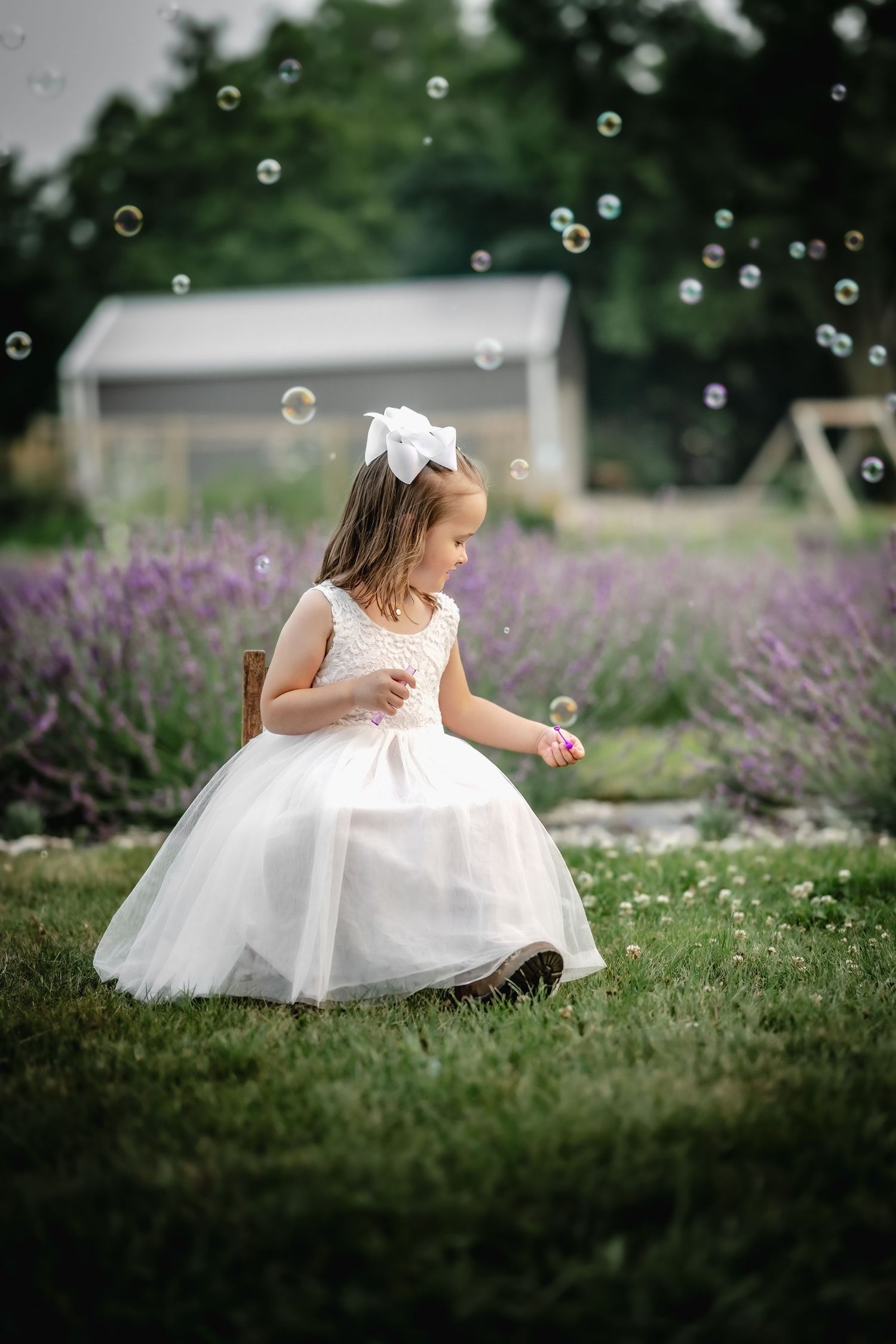 Little girl in elegant white dress playing with bubbles in a lavender garden on a summer day.