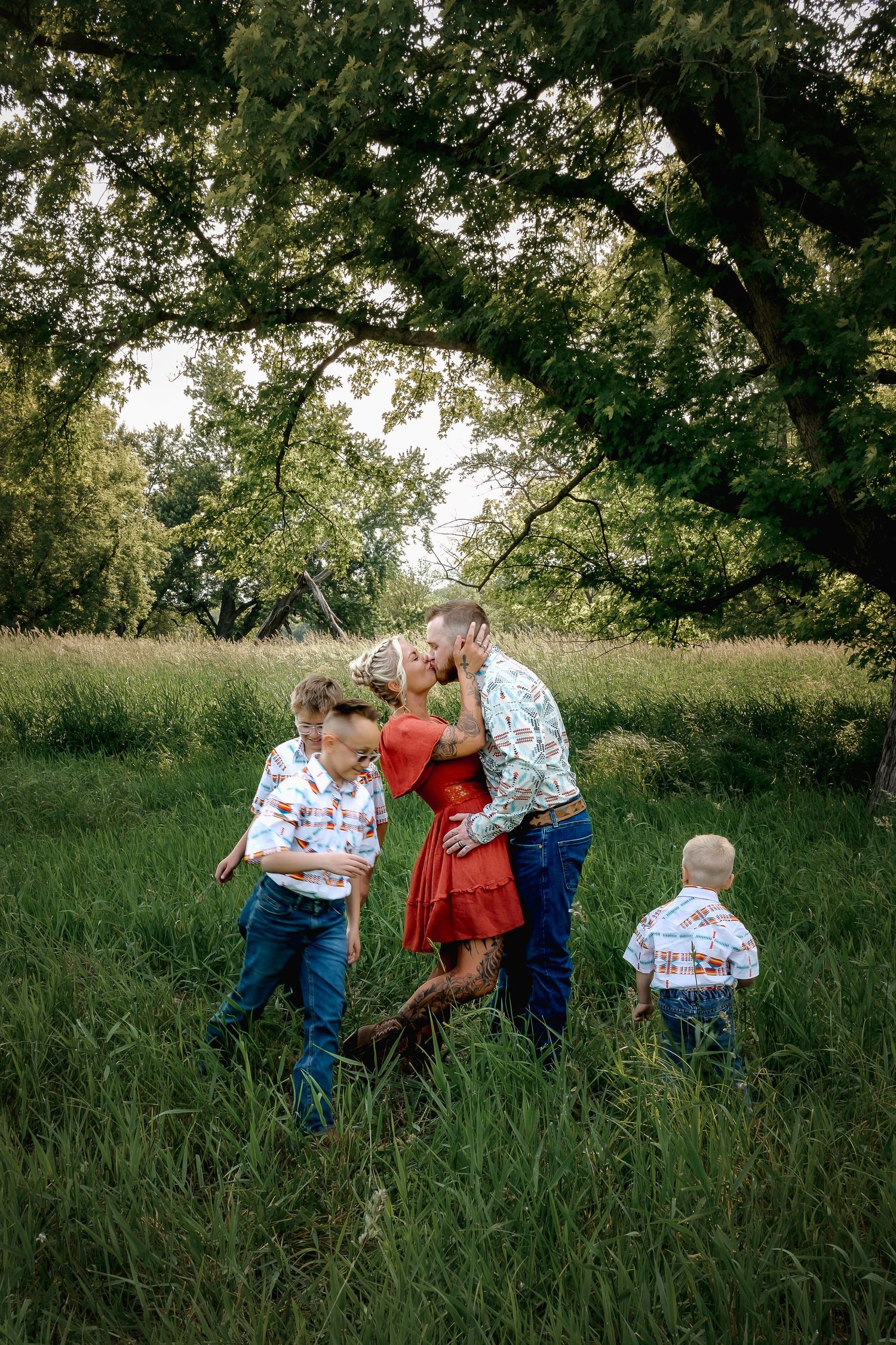 Family with three young boys sharing a kiss in a lush green meadow.