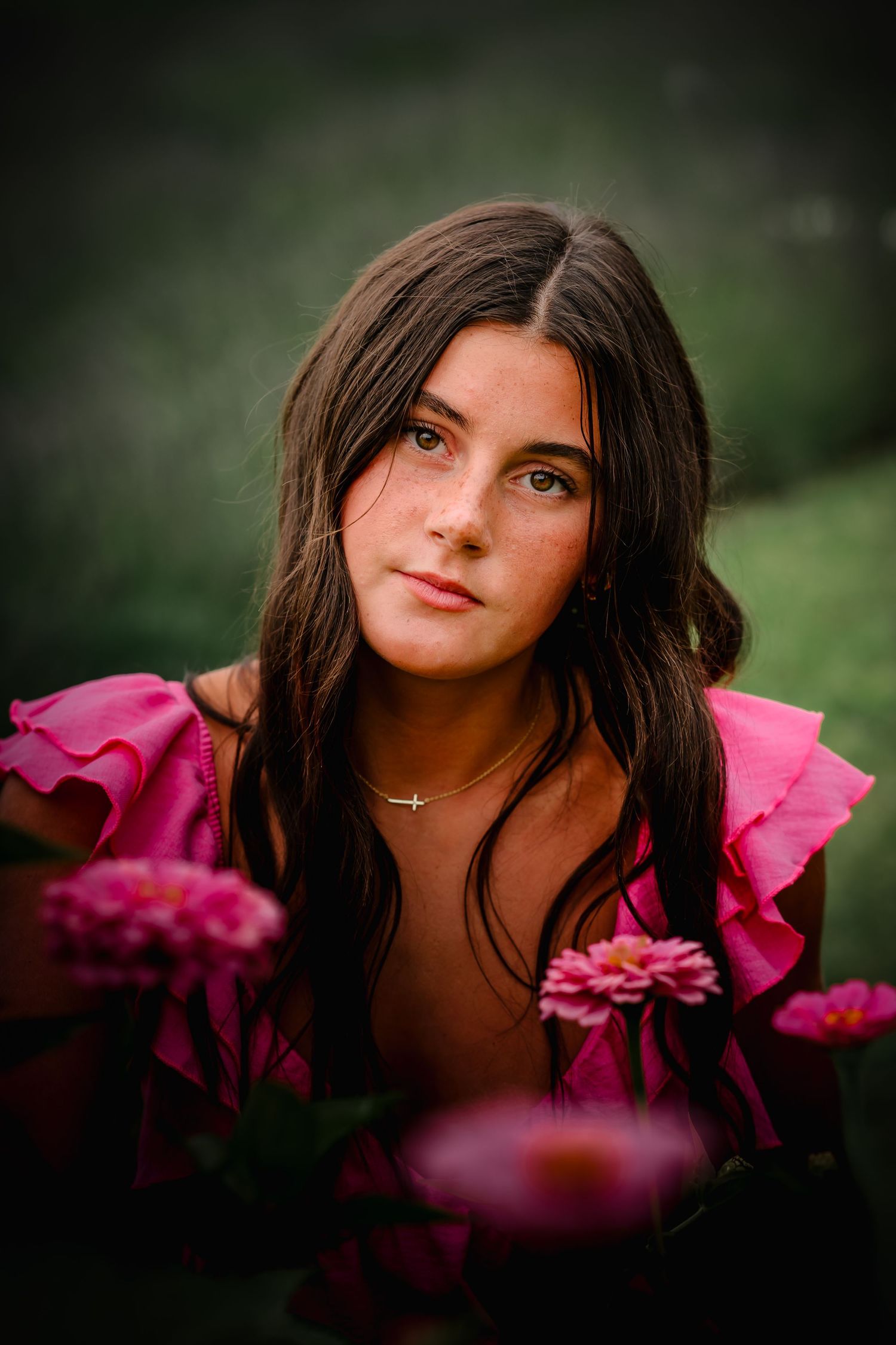 Beautiful brunette teen girl in pink ruffled top surrounded by pink flowers in a garden setting.