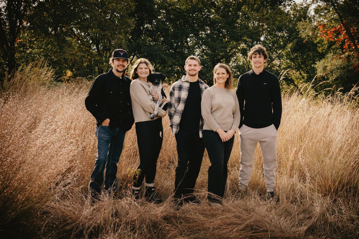 Family of five standing together in a golden wheat field during autumn.