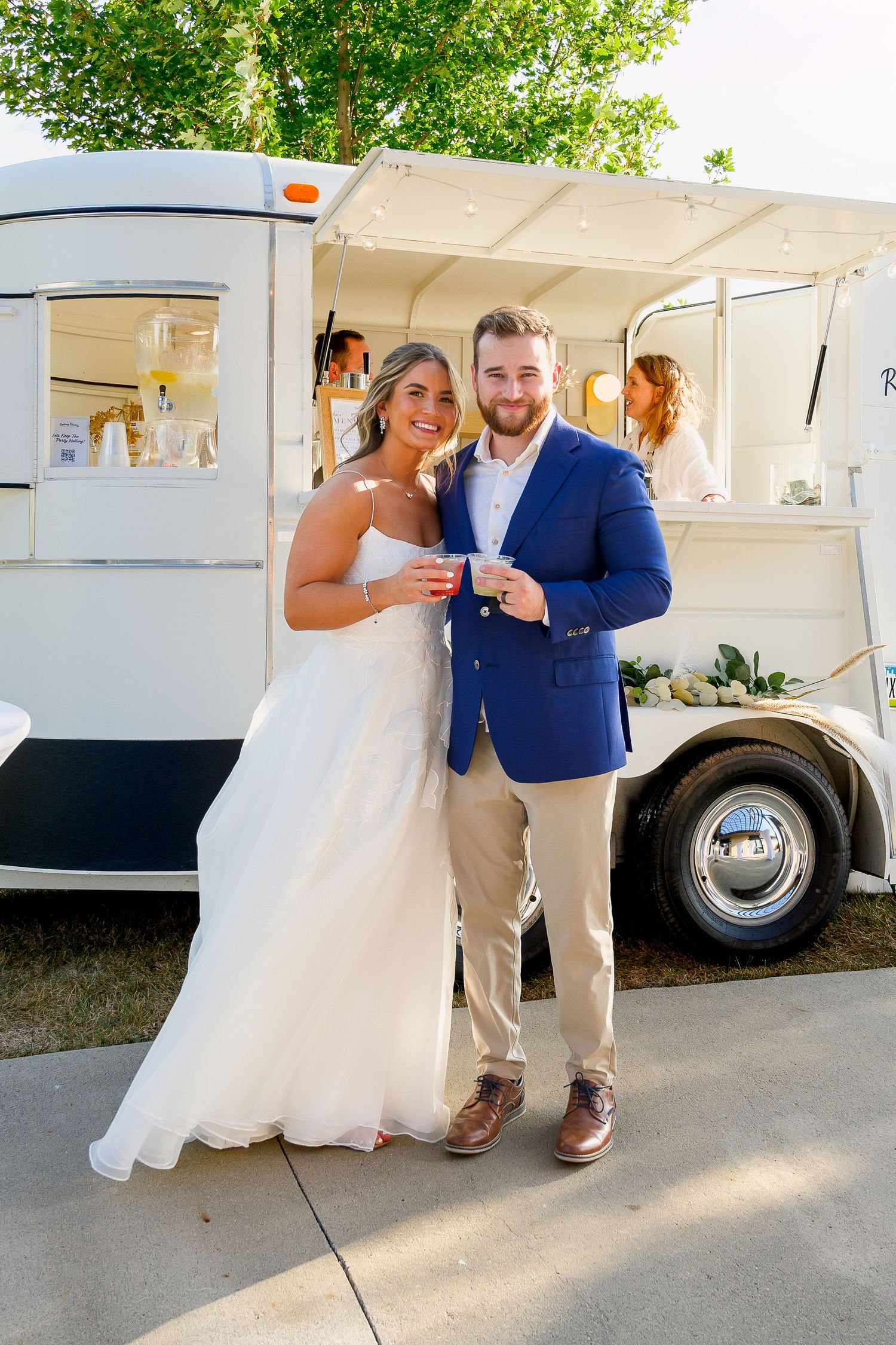 Bride and groom smiling together in front of a white vintage food truck at their outdoor wedding.