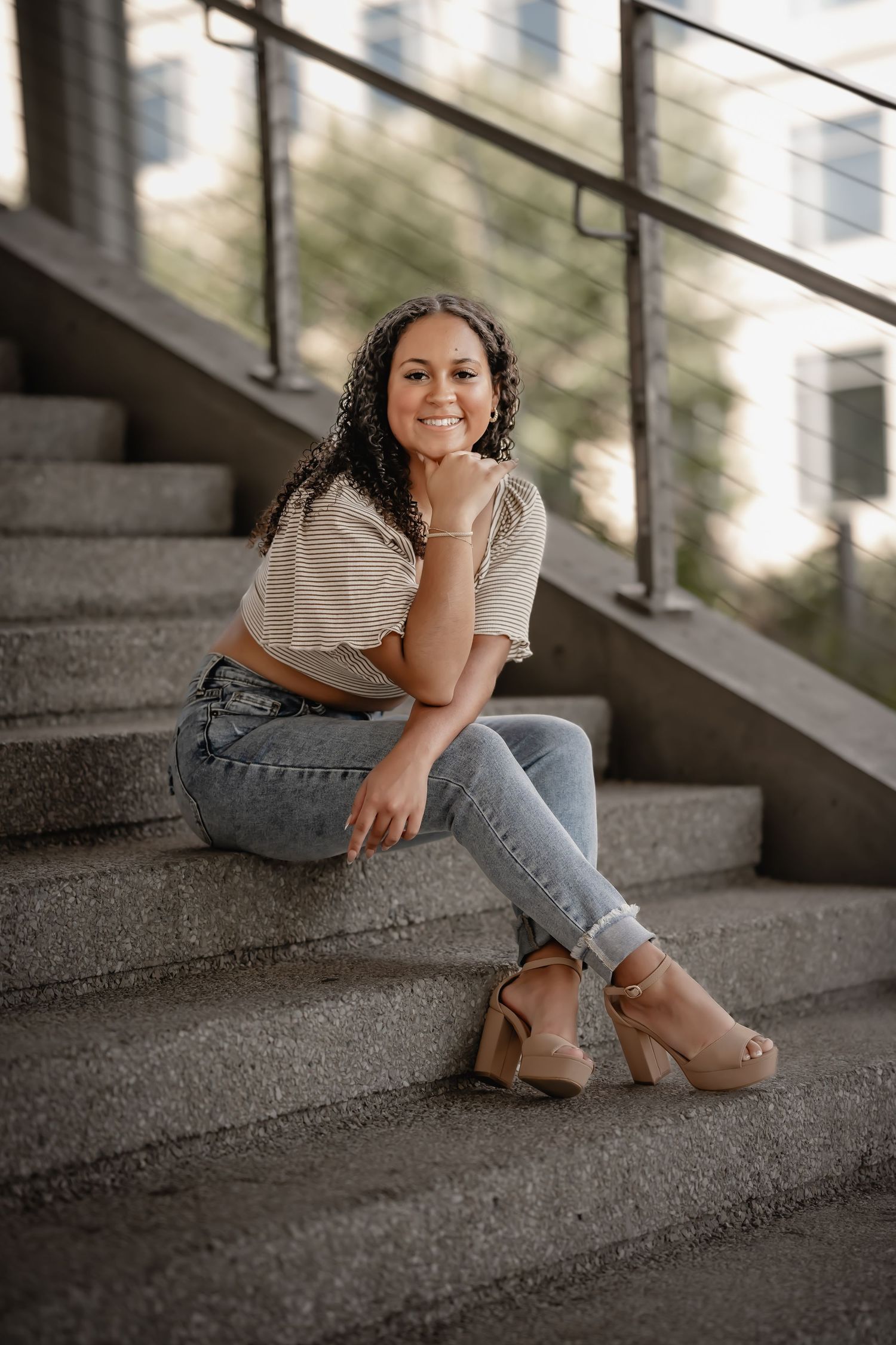 Smiling young woman in striped crop top and jeans sitting on outdoor stone stairs.