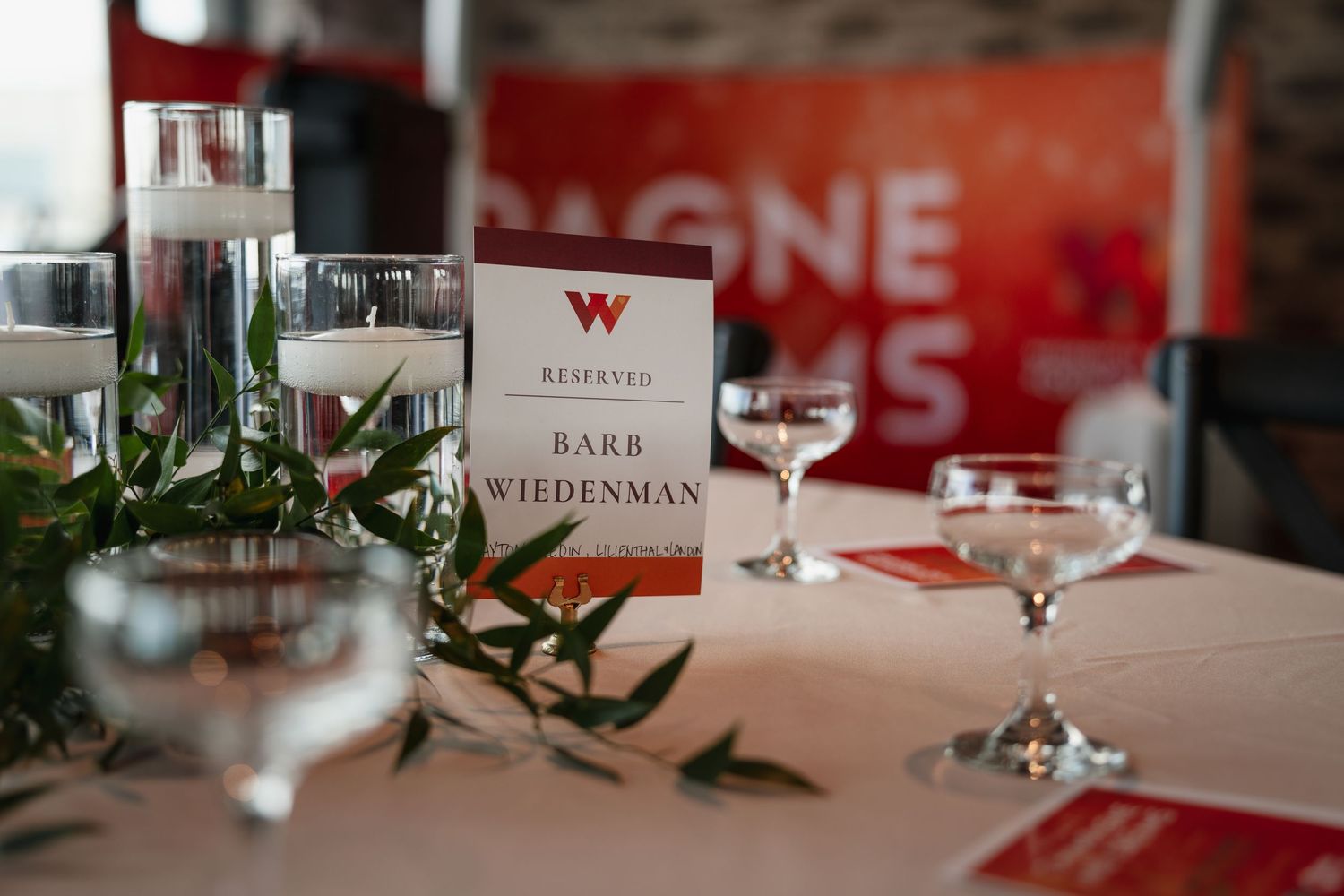 A reserved place card sits on an elegantly set table with candles and greenery.