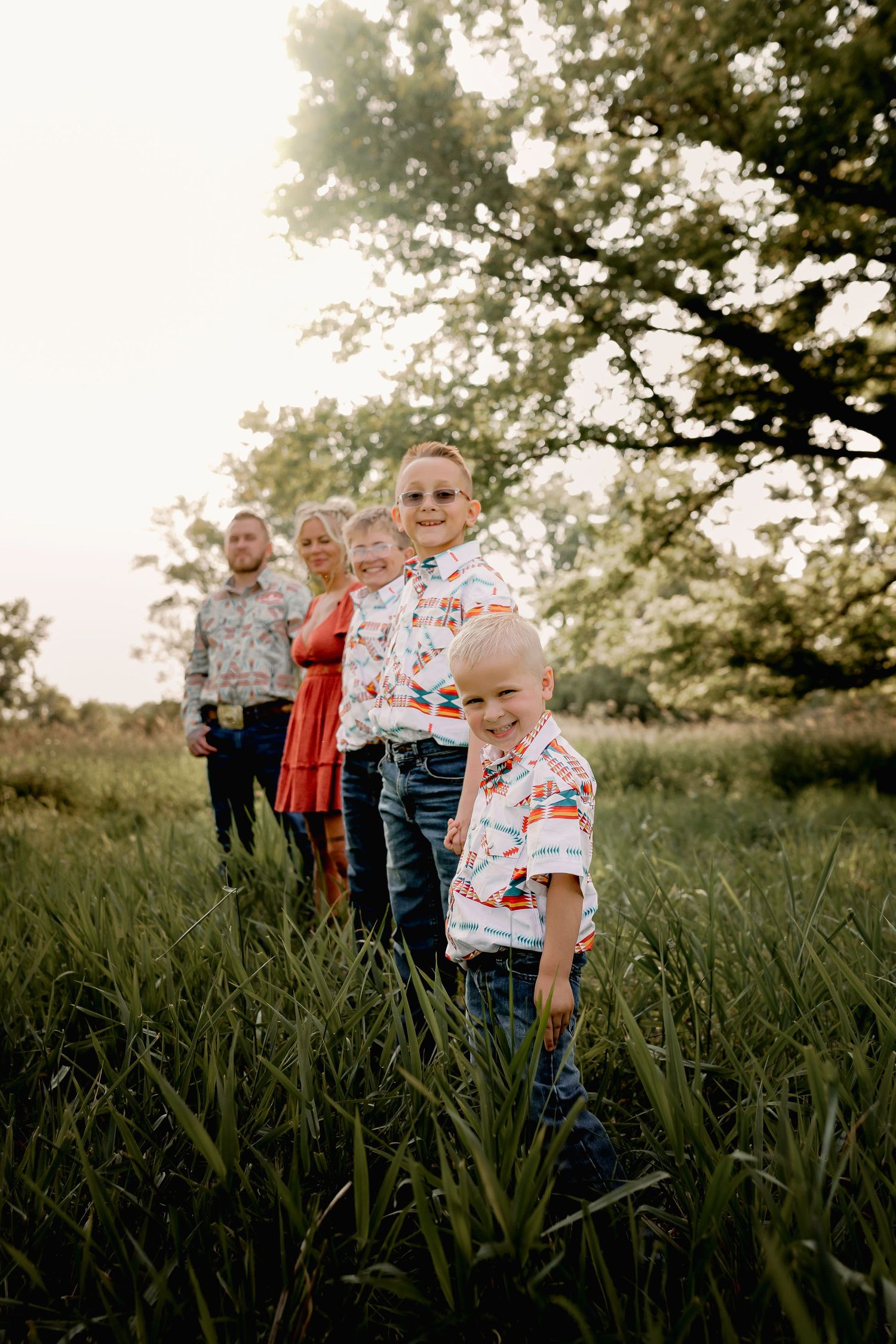 Family of six lined up in a grassy field wearing matching western shirts at sunset.