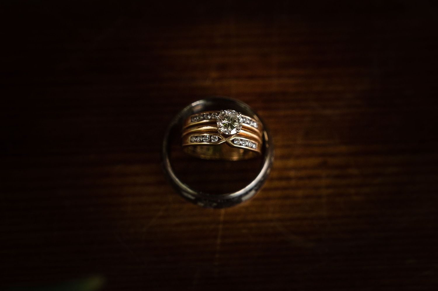 Close-up of stacked gold and diamond wedding rings on a dark wooden surface.