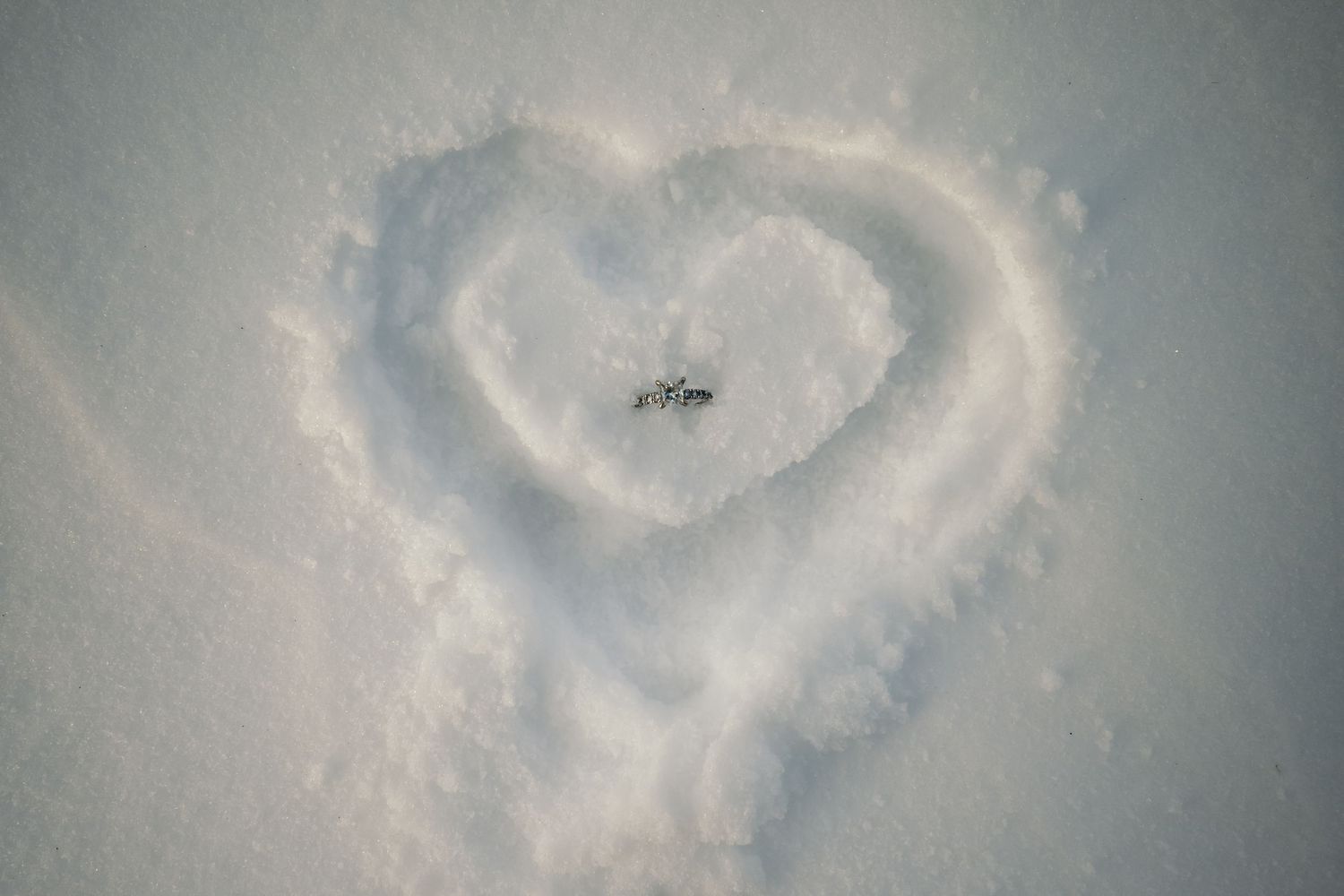 Heart shape drawn in fresh white snow, romantic winter engagement photo session.