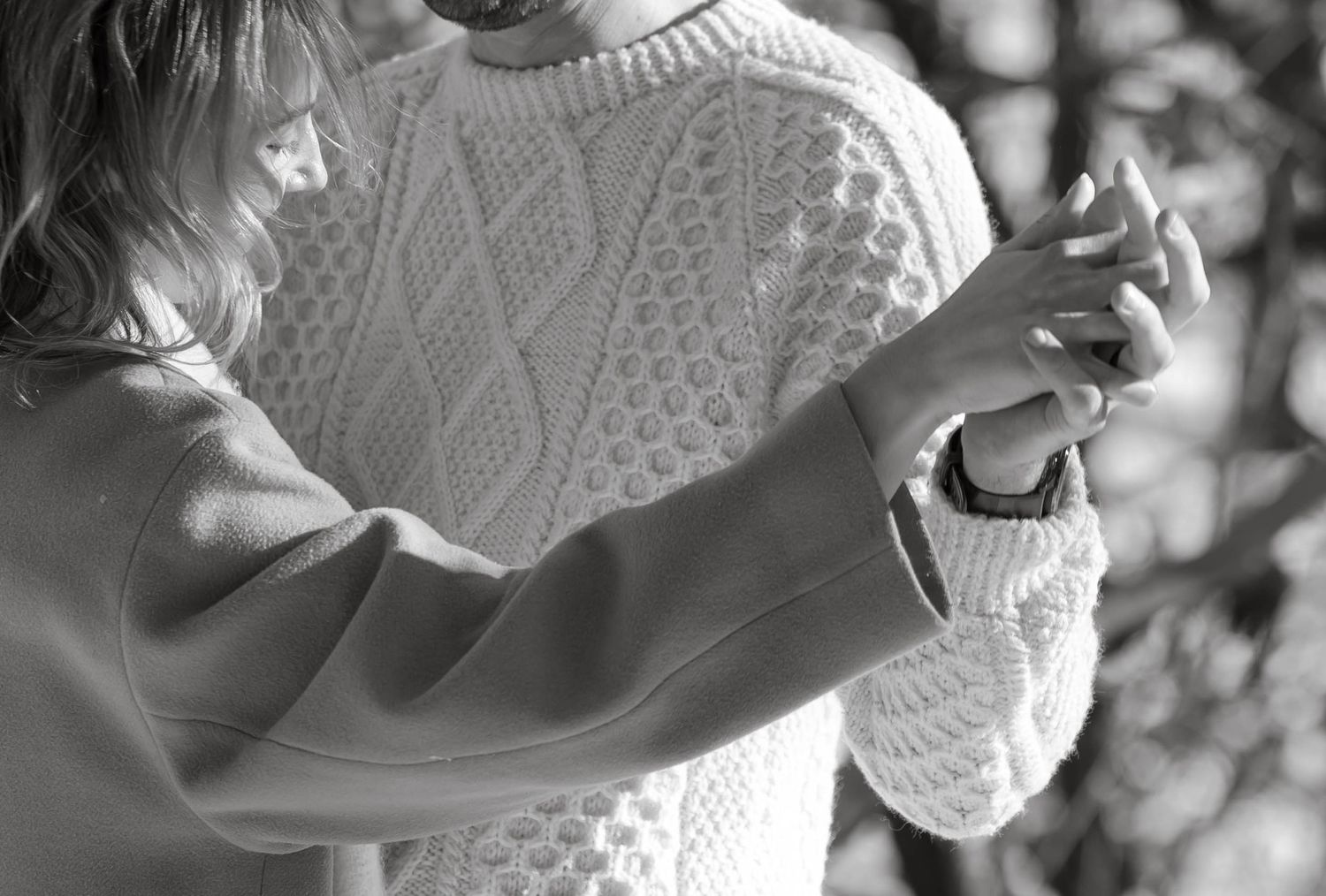 Black and white detail shot of hands intertwined against a cable knit sweater background.