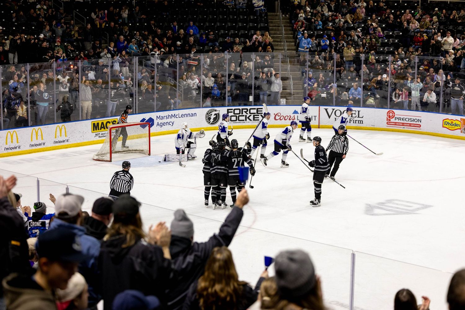 Wide shot of a hockey arena with crowd cheering during an exciting game moment.