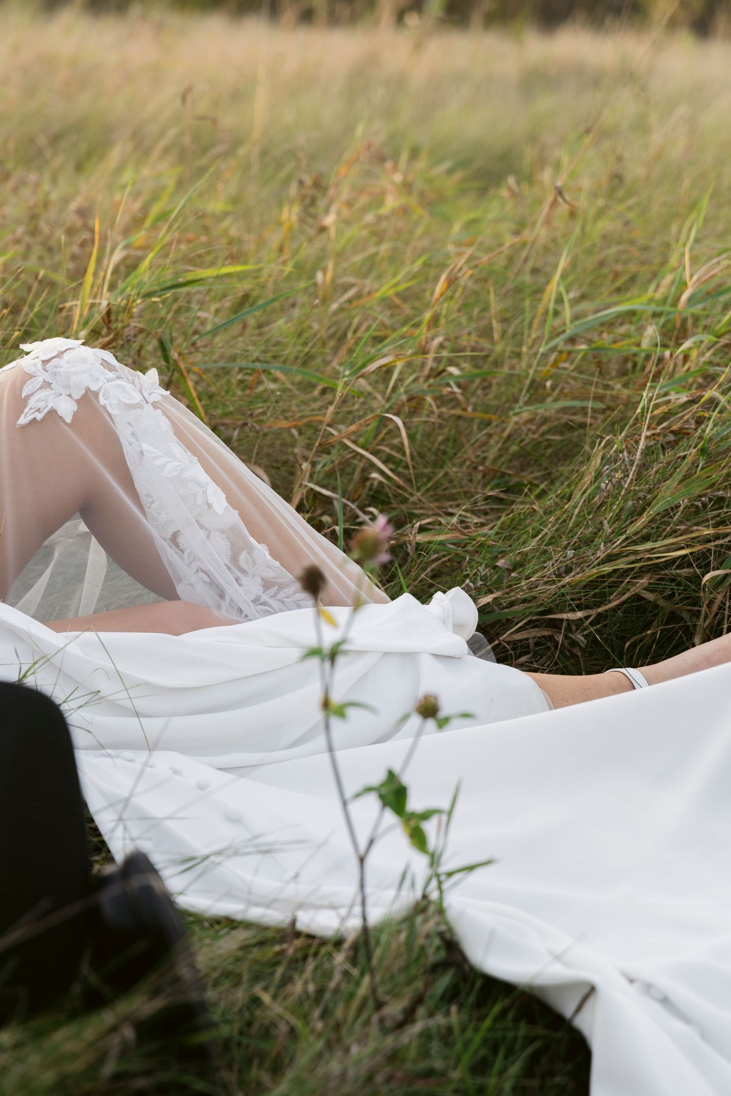 Close-up details of a white lace wedding dress flowing in tall grass during an outdoor photo session.