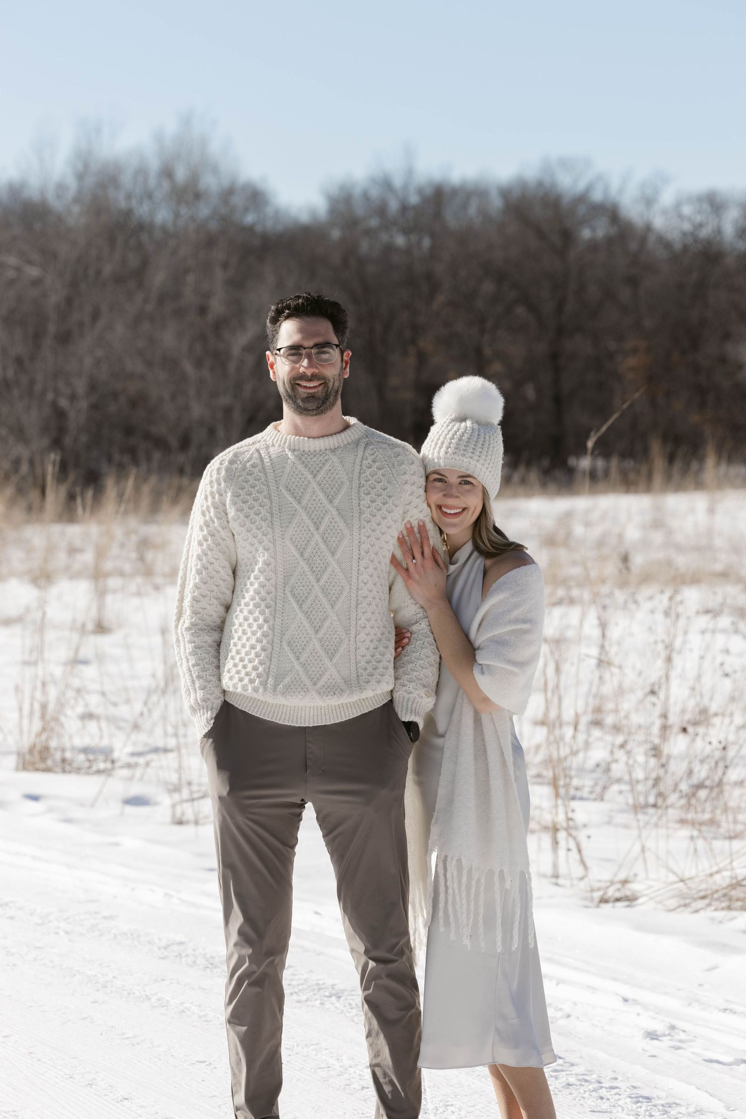 A winter portrait of a couple in coordinated neutrals standing in a snowy field.