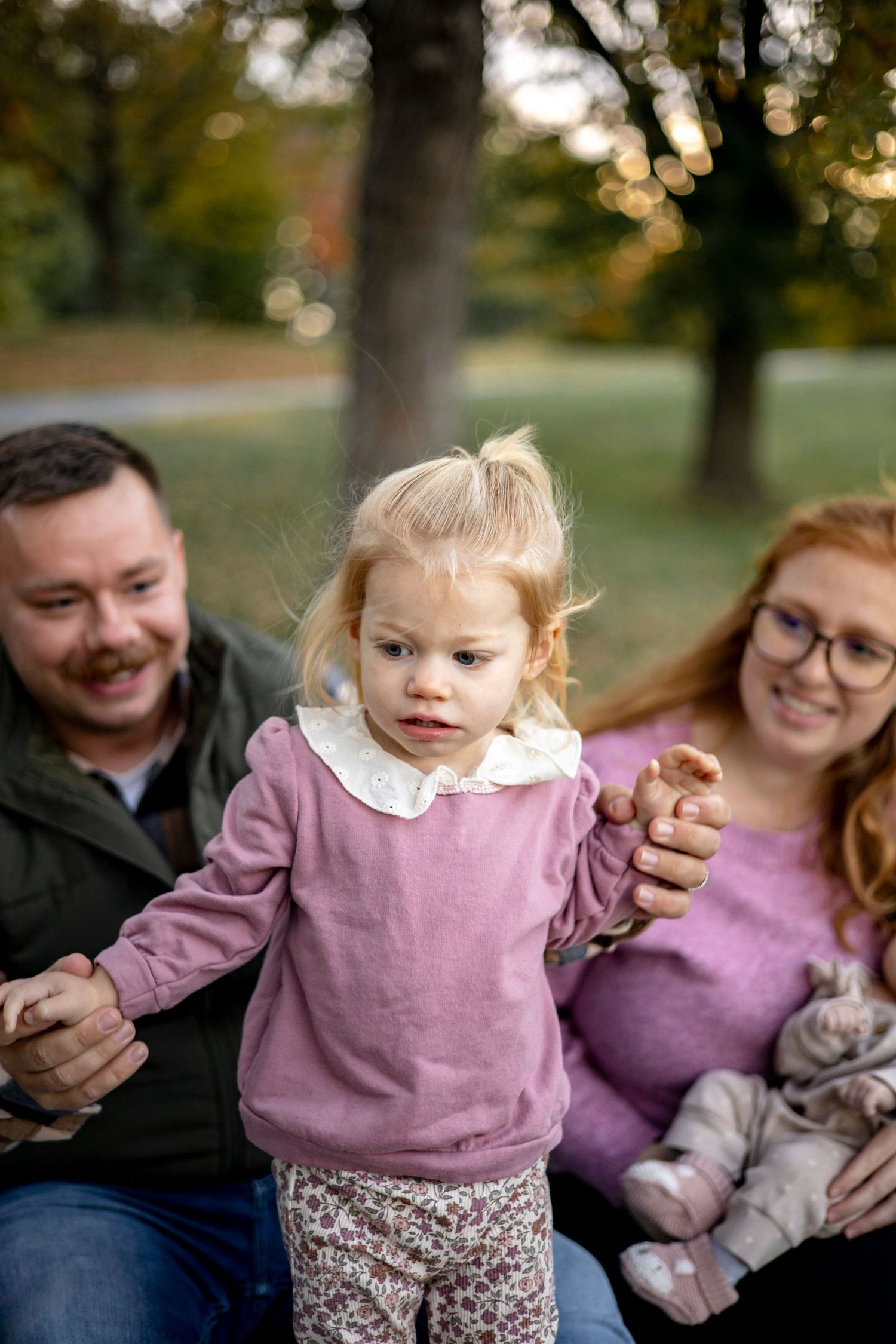 A family sits together on autumn grass sharing a tender moment.