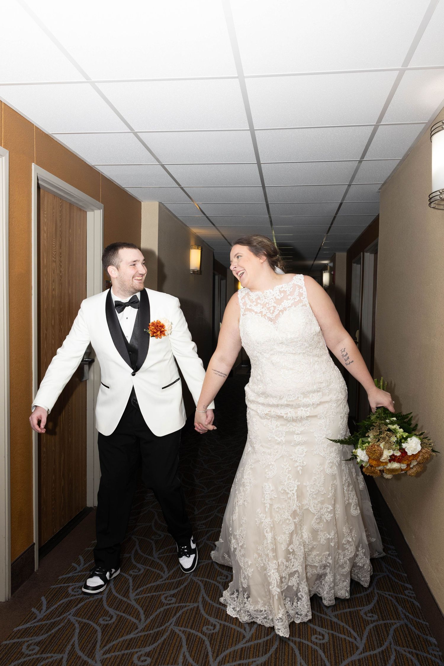 Candid moment of newlyweds laughing while walking down hotel hallway.