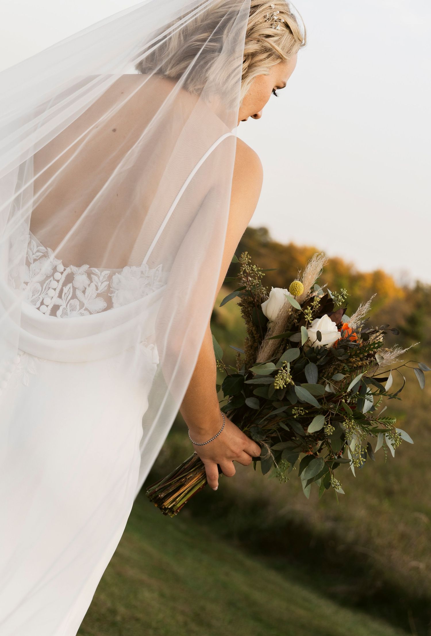 Bride holding a rustic bouquet with flowing veil in golden afternoon light.