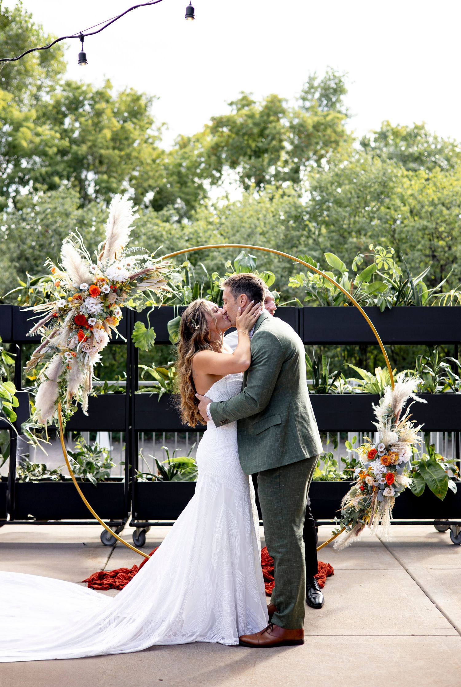 A wedding ceremony moment under a floral arch with white and orange blooms.