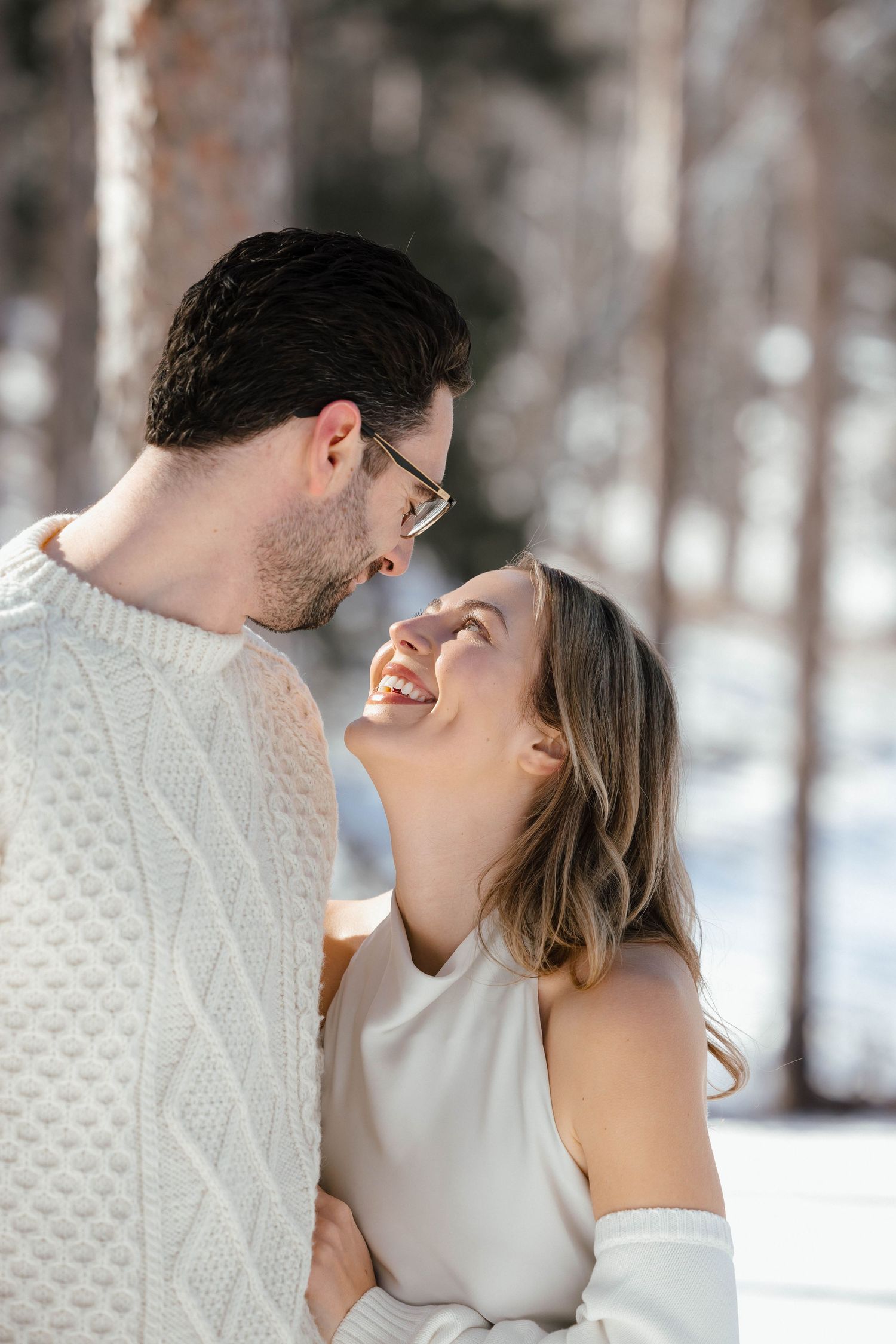 Joyful couple laughing together in a winter forest setting.