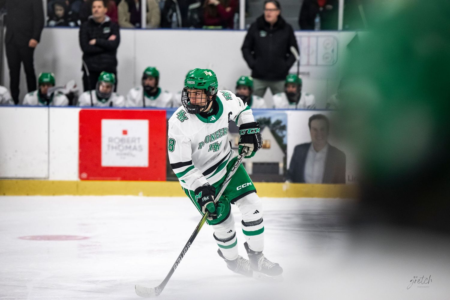 Hockey player in green jersey skates with the puck during competitive game action.