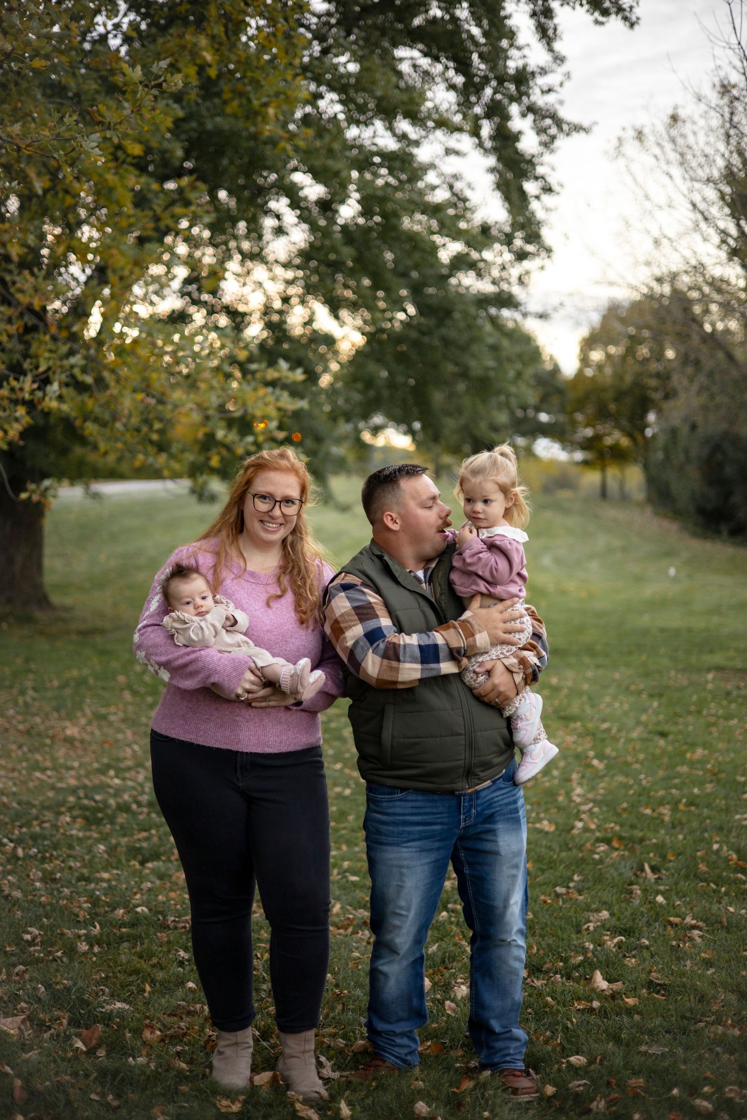 A family group poses together on grass during an autumn outdoor photo session.