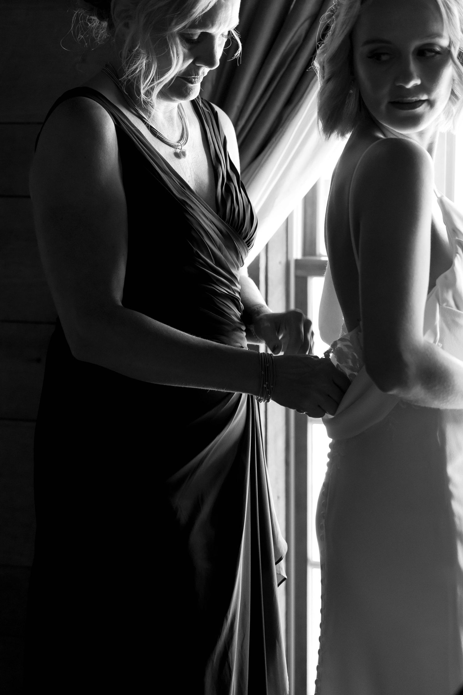 Dramatic black and white photo of wedding preparation with backlit silhouettes.