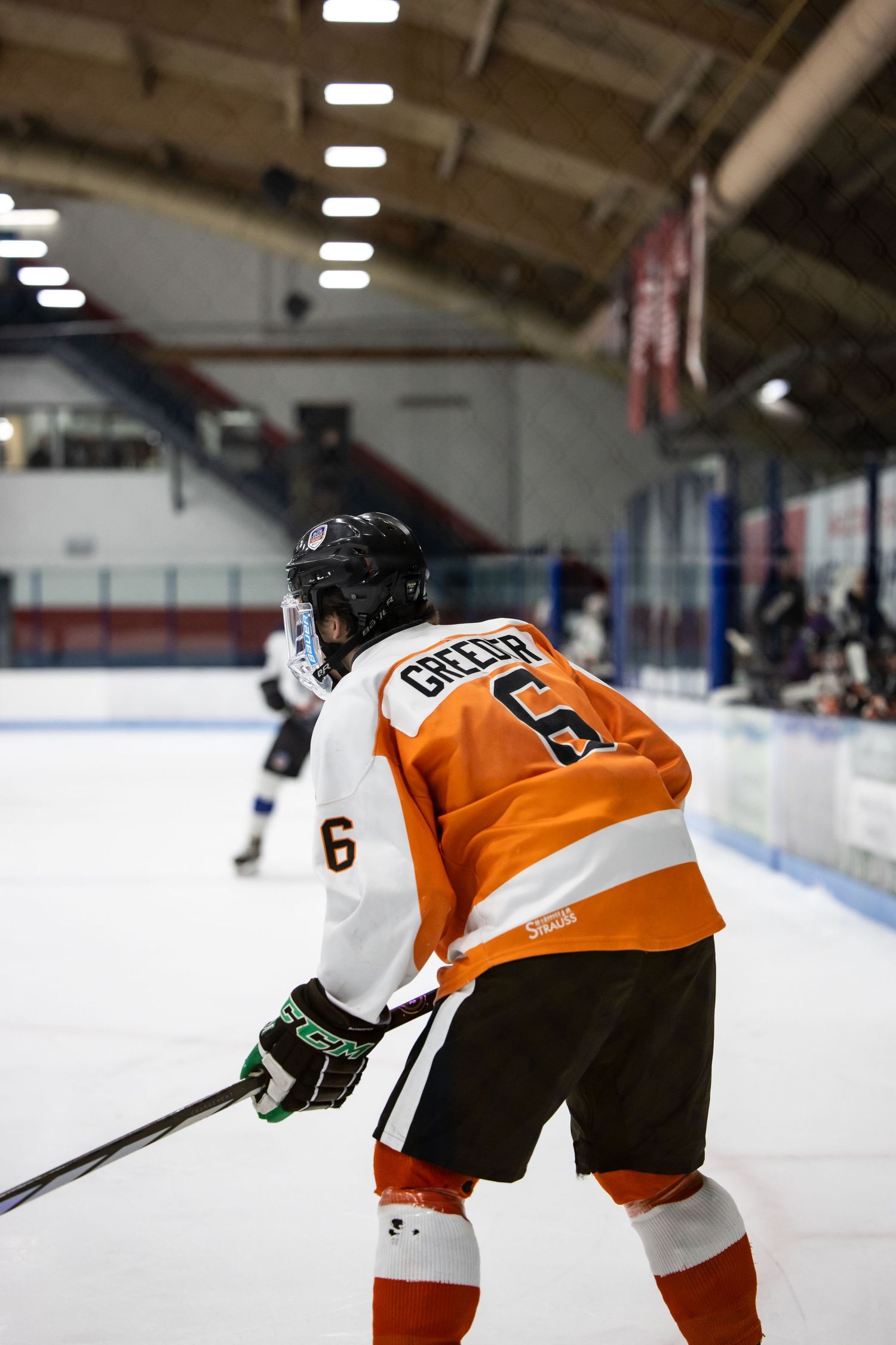 Hockey player in orange jersey skating on ice rink during competitive match.
