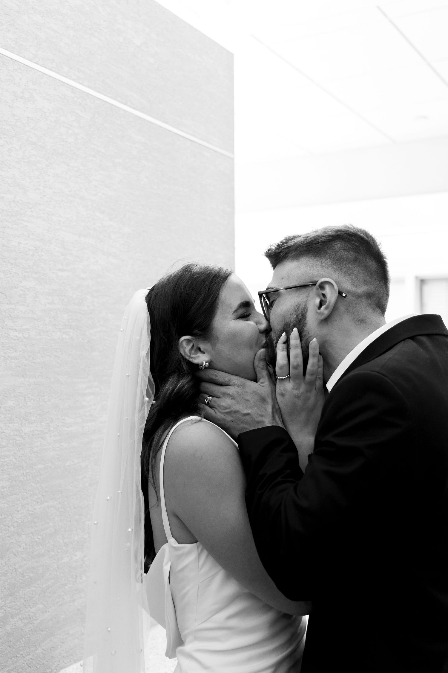 An intimate black and white portrait of a wedding couple against a white wall.