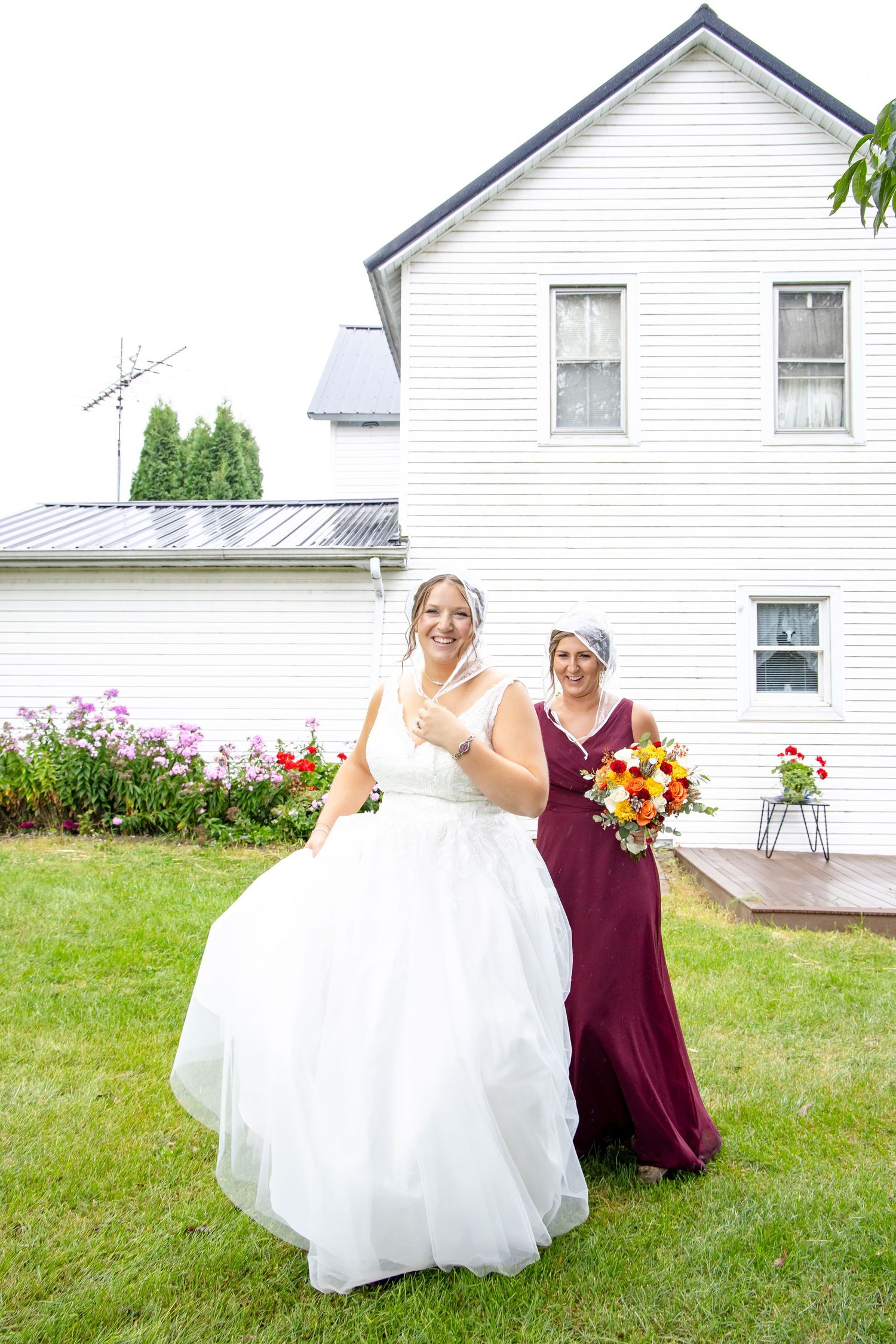 A wedding scene in front of a white farmhouse with blooming garden flowers.