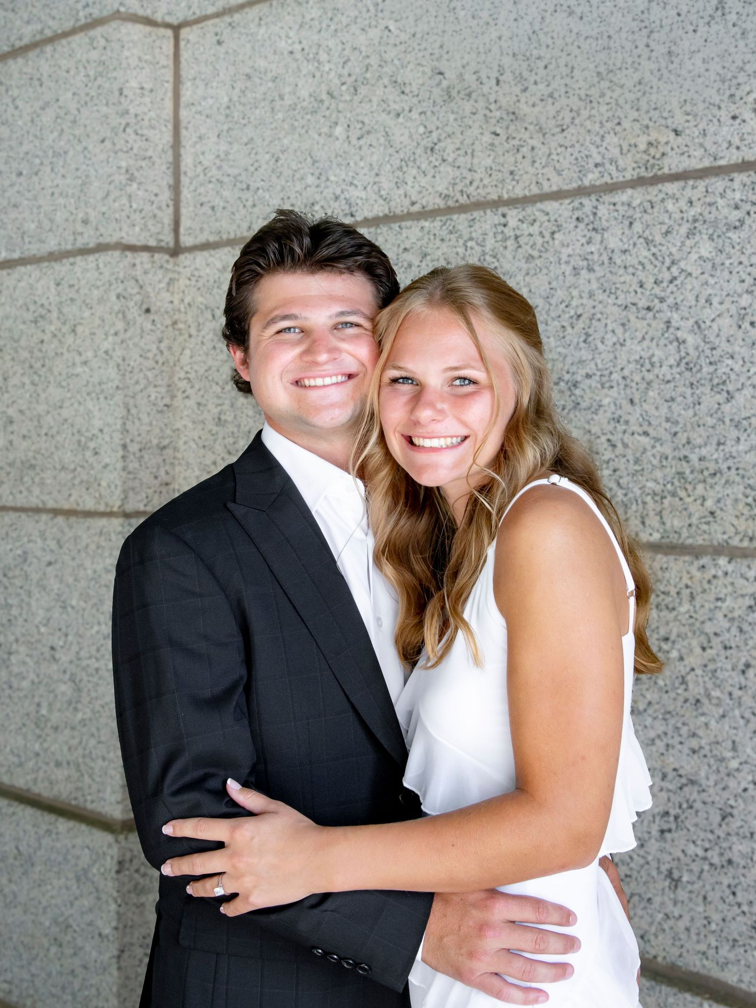 Happy couple in formal wear sharing intimate moments against a stone wall.