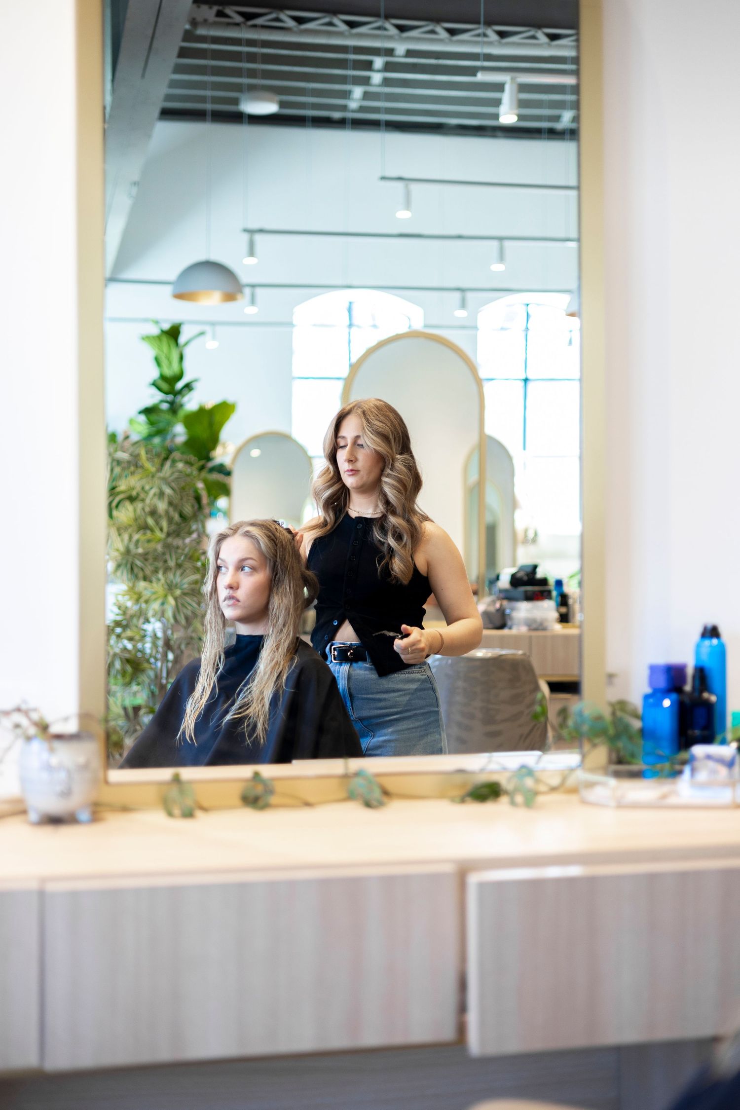 Modern salon interior with mirror reflection showing styling session and arched architectural details.