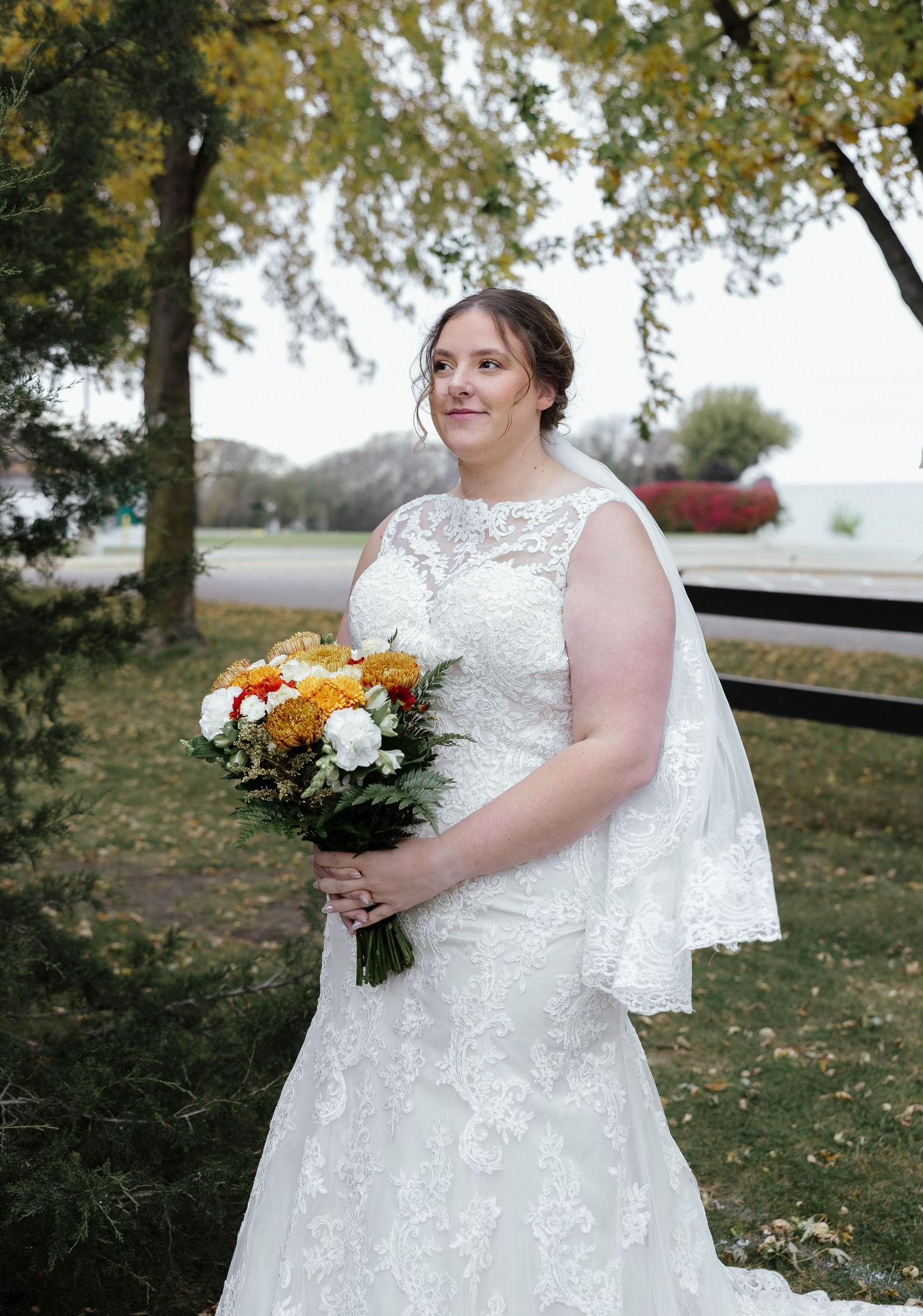 A wedding portrait outdoors featuring a lace dress and autumn-colored bouquet.