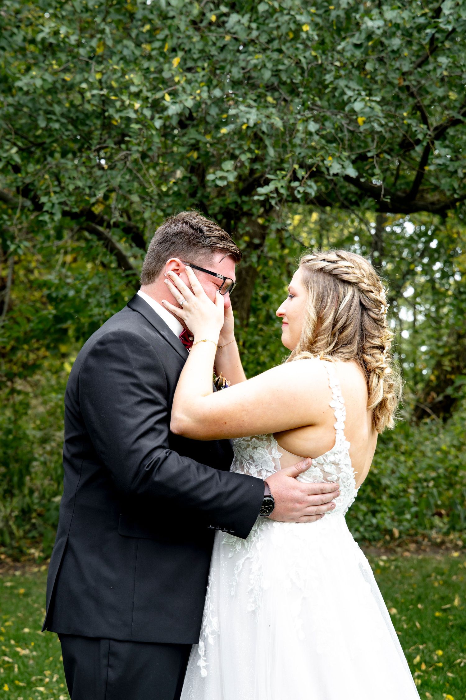A joyful wedding couple shares a romantic moment together outdoors surrounded by green foliage.