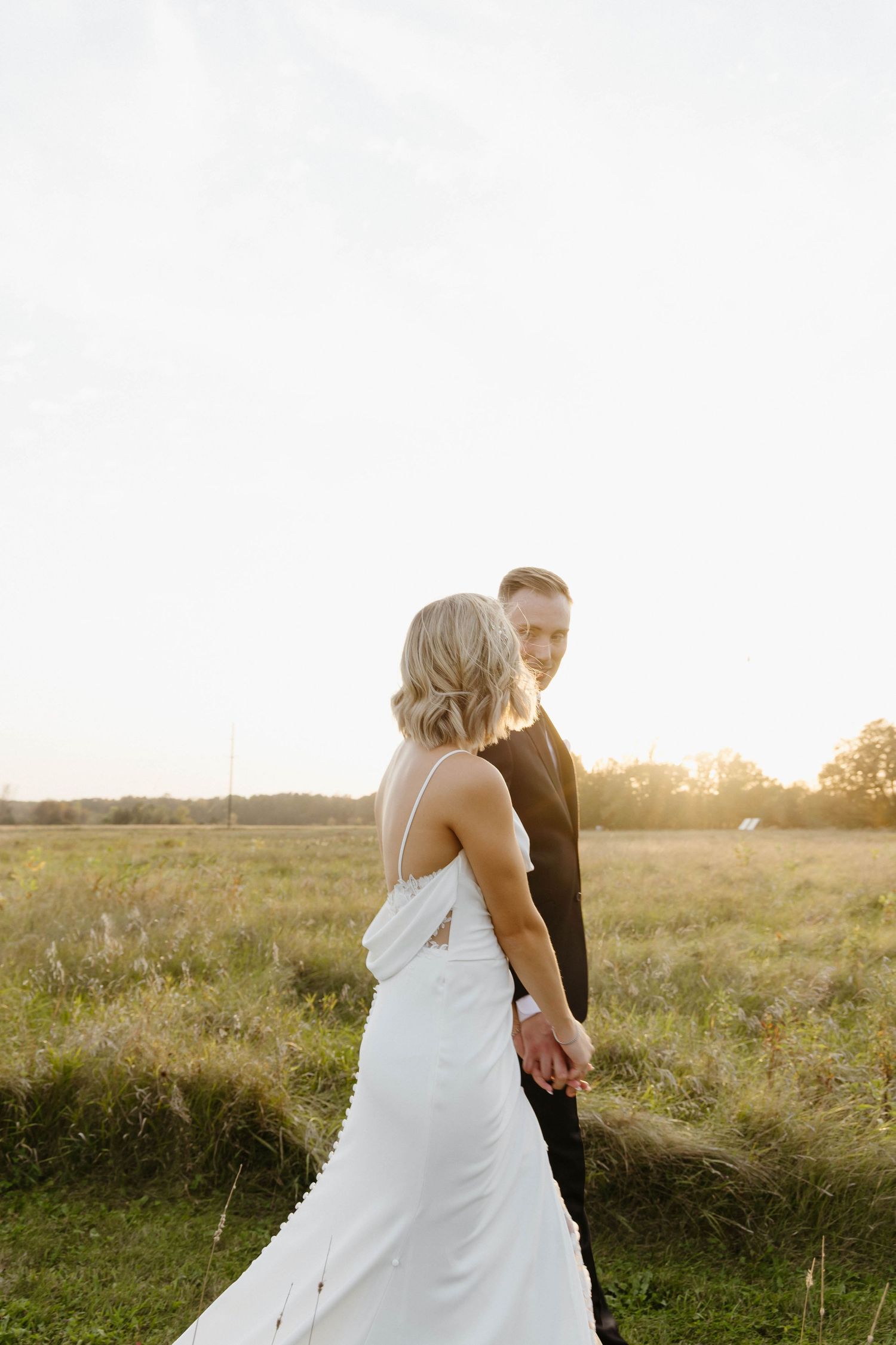Newlyweds embracing in sunlit field during golden hour photography session.