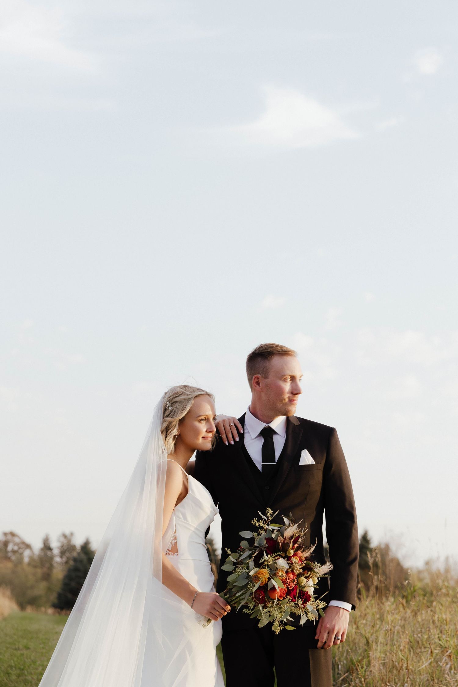 Wedding couple embracing in golden field during sunset portrait session.