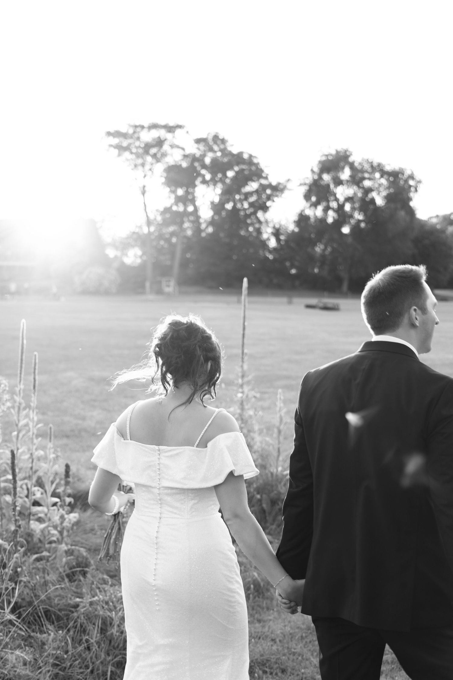 Wedding couple walking through field with wildflowers at dusk.