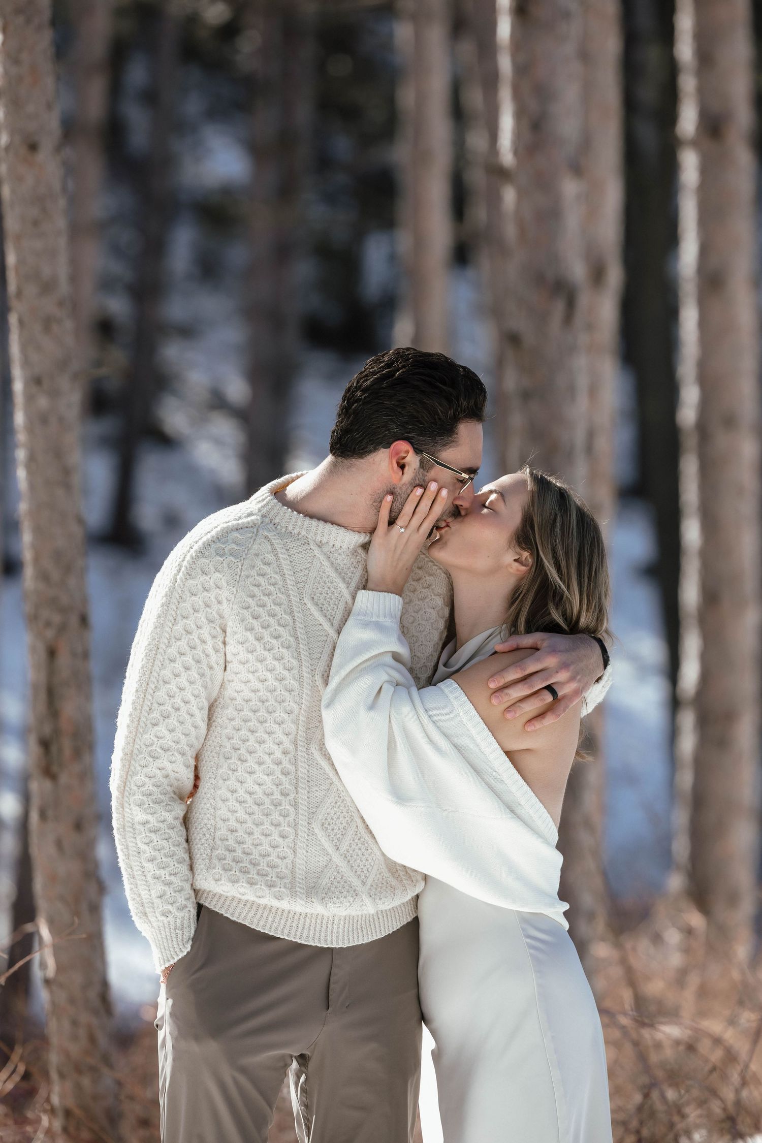 Romantic winter forest scene with couple in coordinated white and beige outfits.