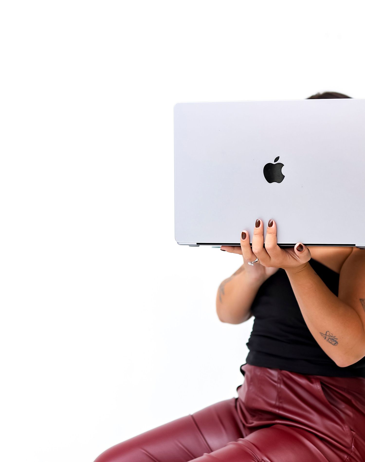 Someone holds a silver MacBook laptop while wearing burgundy leather pants.