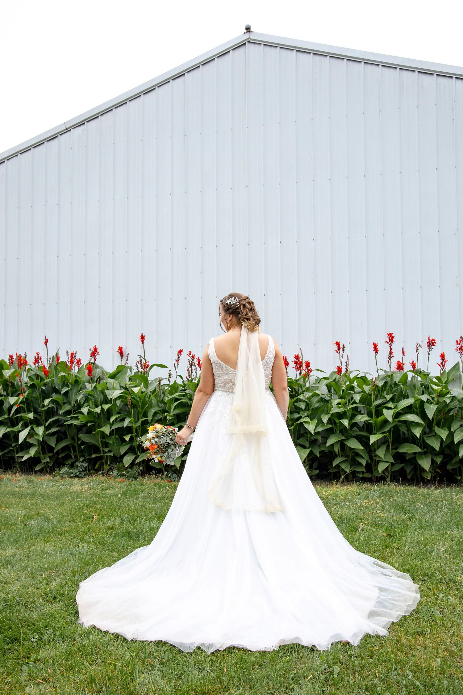 A bride in a flowing white gown poses near red tulips against a light blue wall.