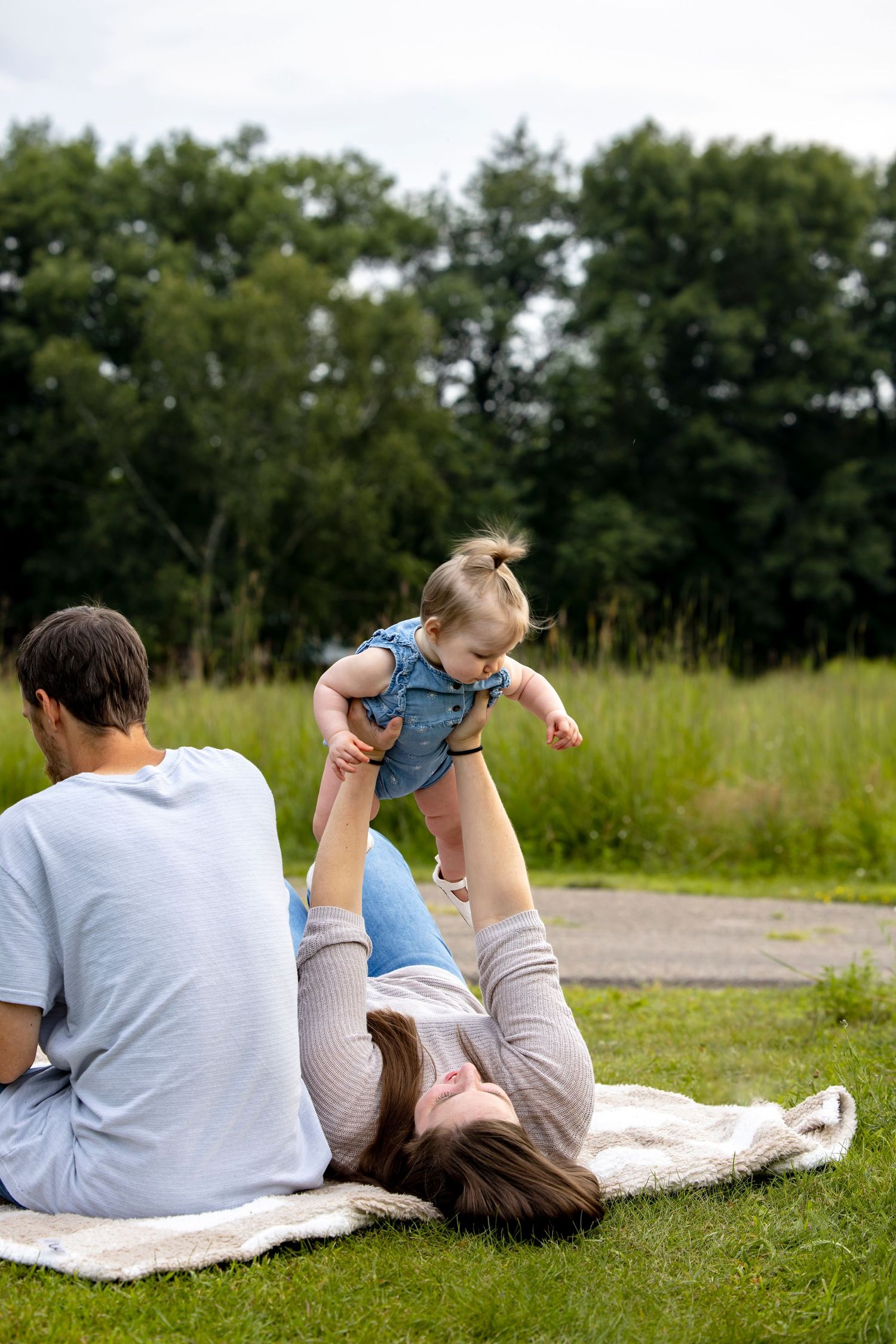 Family relaxing together on blanket in grassy field on sunny day.