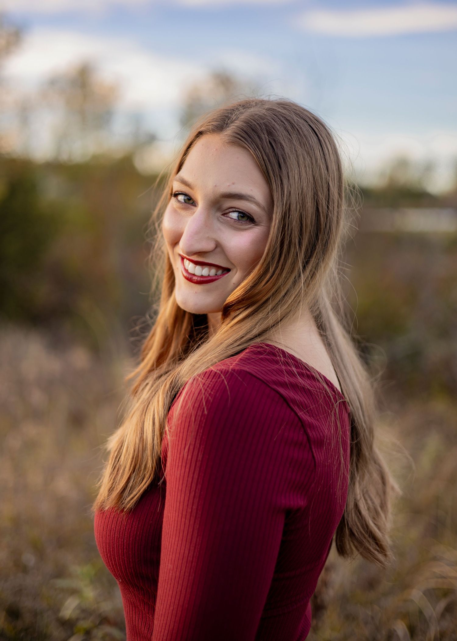 Person in burgundy sweater poses outdoors during autumn photoshoot with natural lighting.