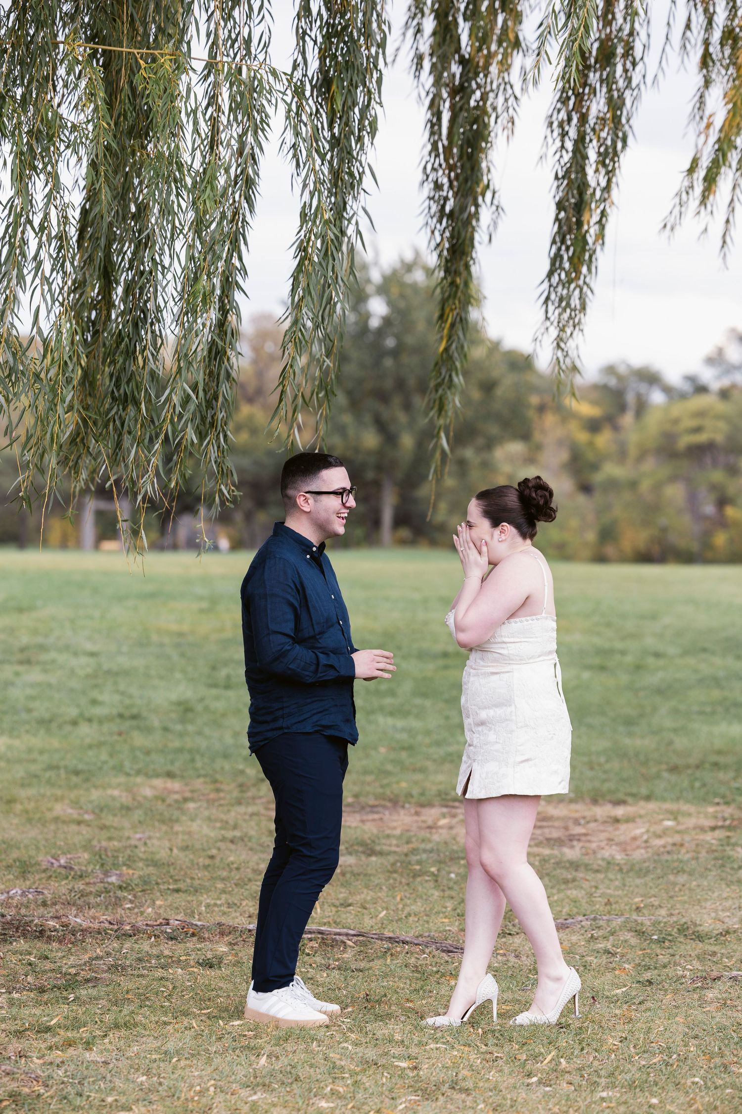 Couple sharing a surprise proposal moment under a weeping willow tree.