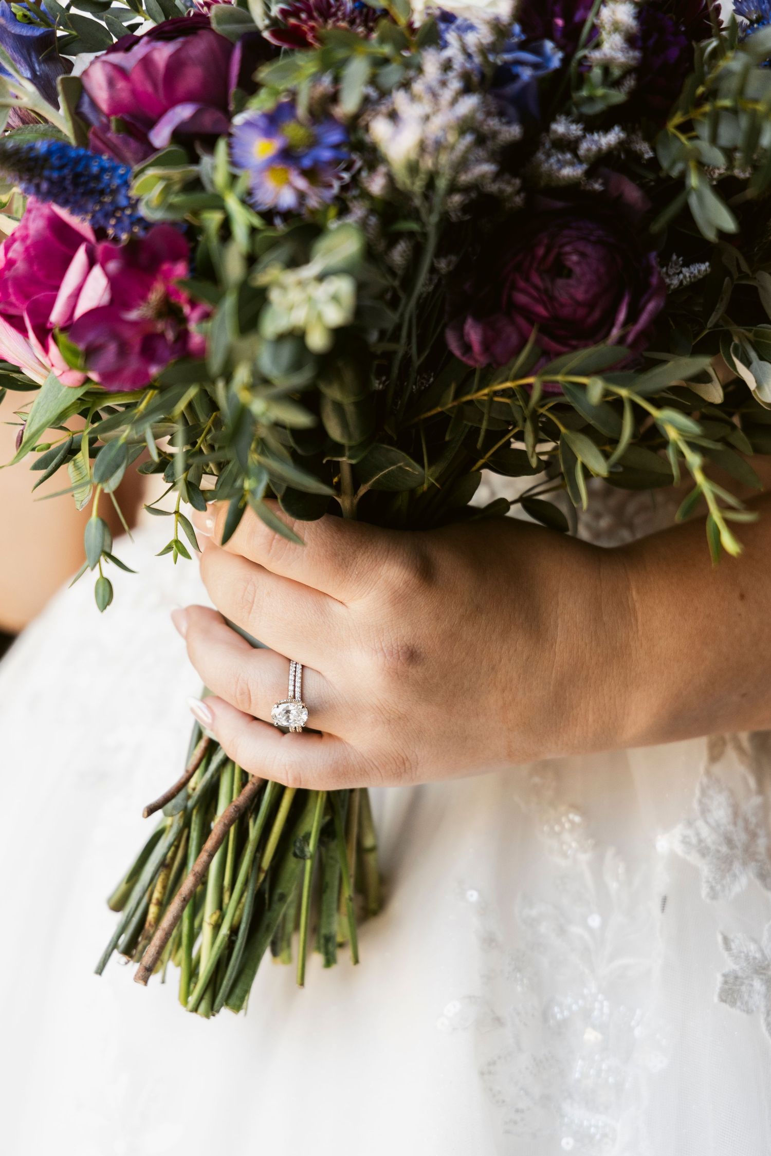 Close-up of vibrant purple and pink wedding bouquet held against white wedding dress.