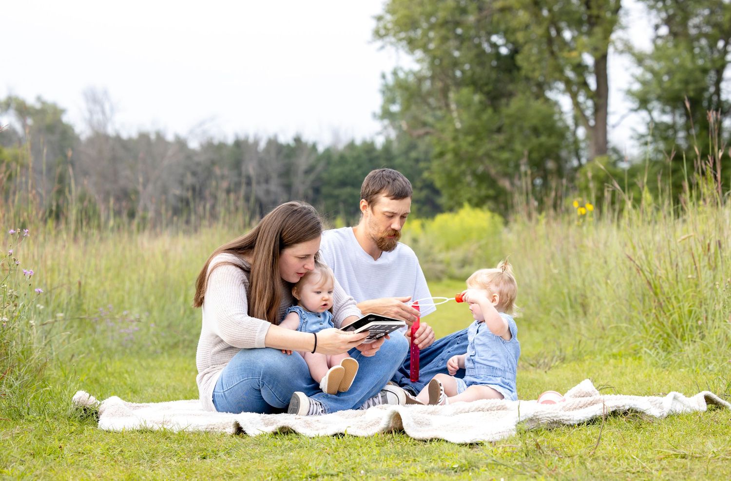 Family enjoying a relaxing day on a blanket in a sunny meadow.