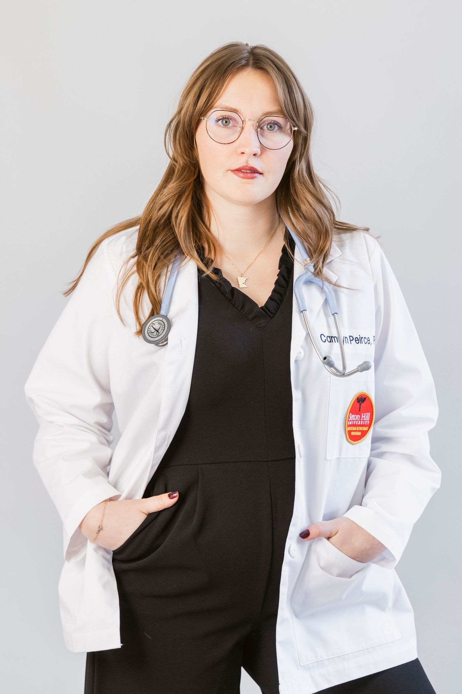 Healthcare professional in white coat and black top poses for professional headshots against light background.
