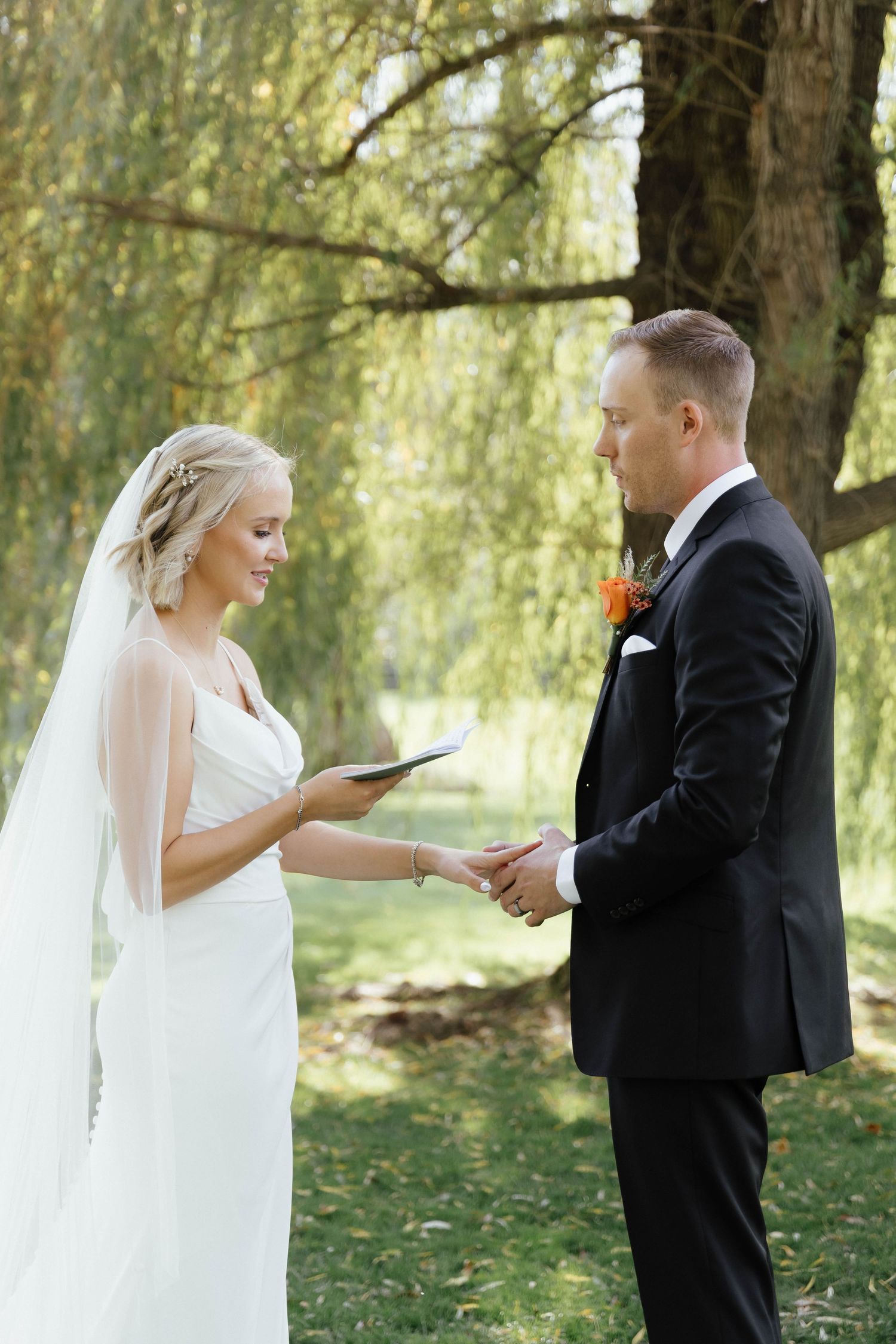 Couple exchanging letters during their first look moment under weeping willow trees.