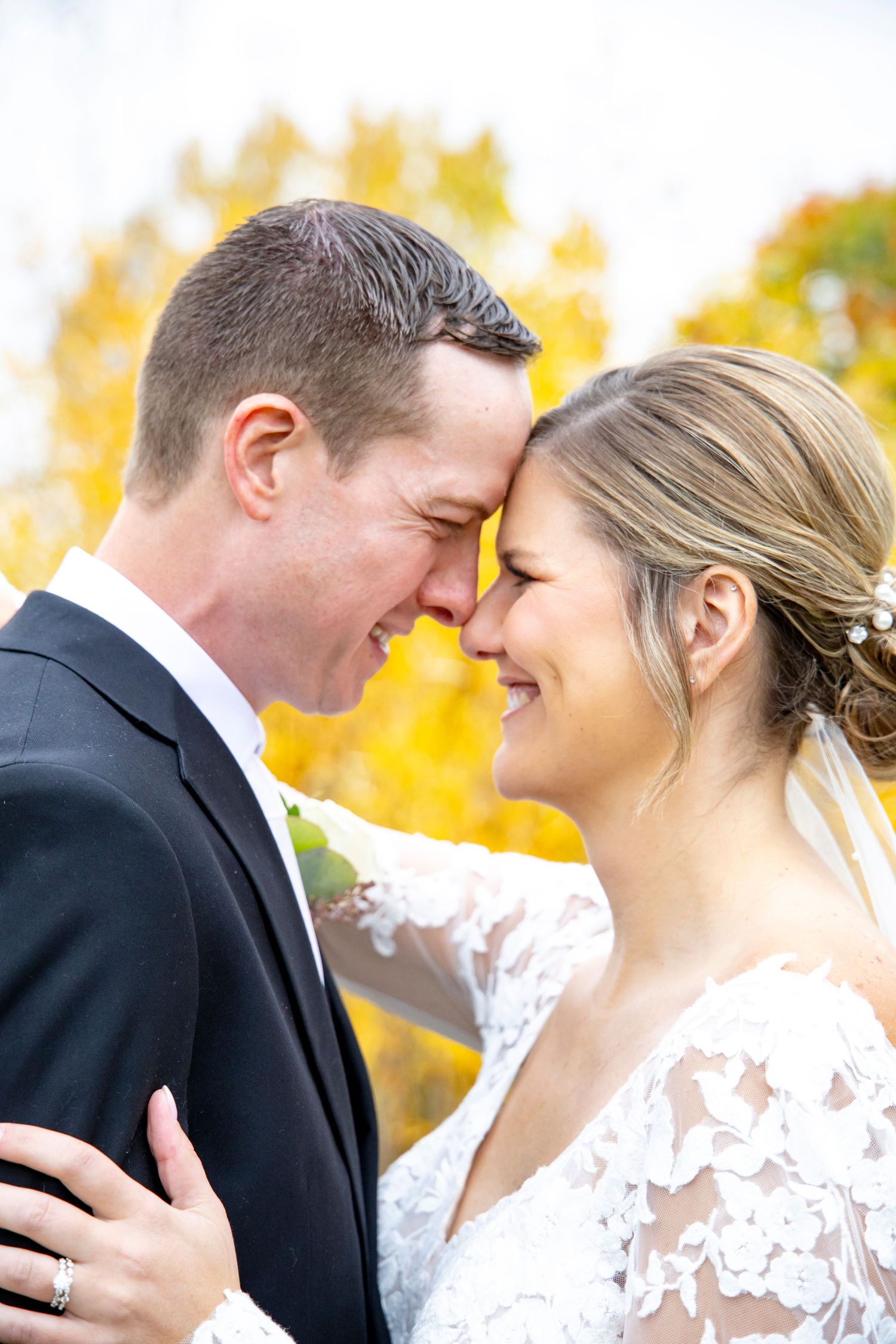 A romantic wedding portrait showing a tender moment between newlyweds against a golden autumn background.