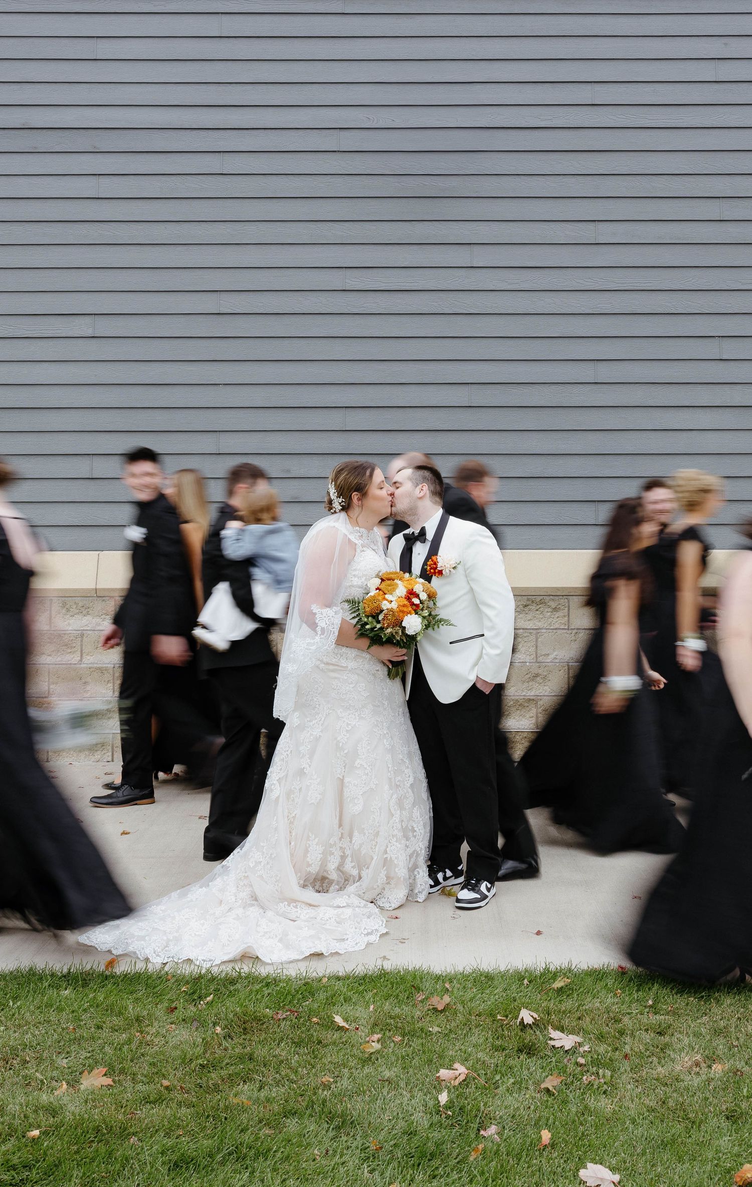 Romantic moment between newlyweds while wedding party passes in background.