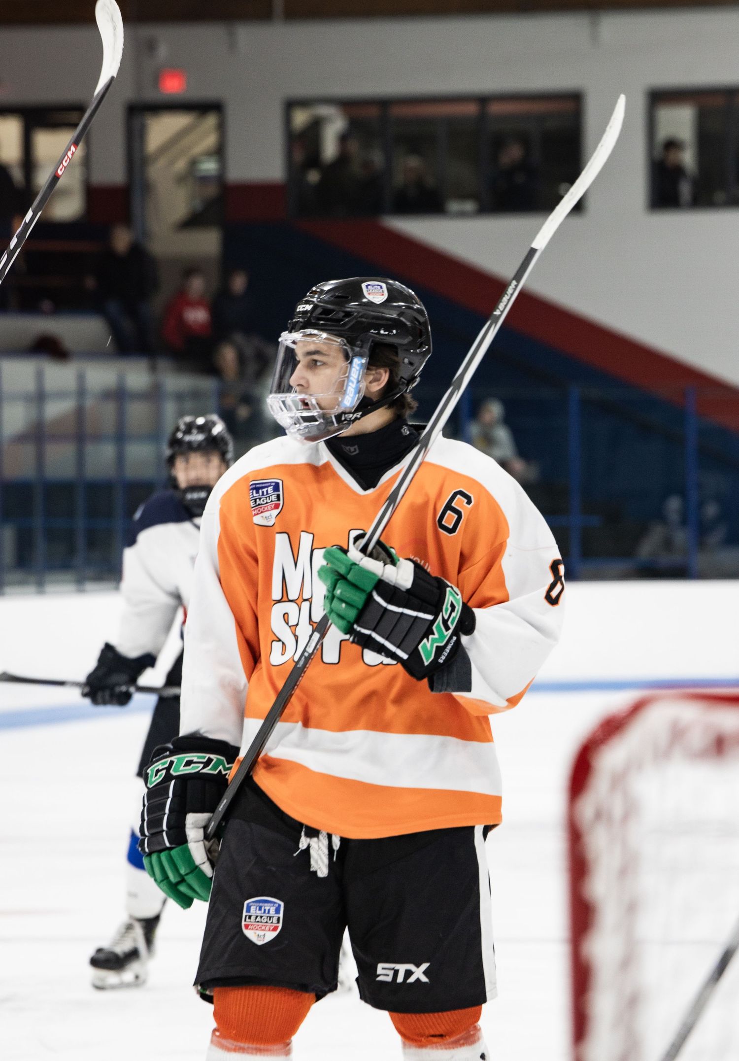 Hockey players in orange and white jerseys compete during an intense game moment.