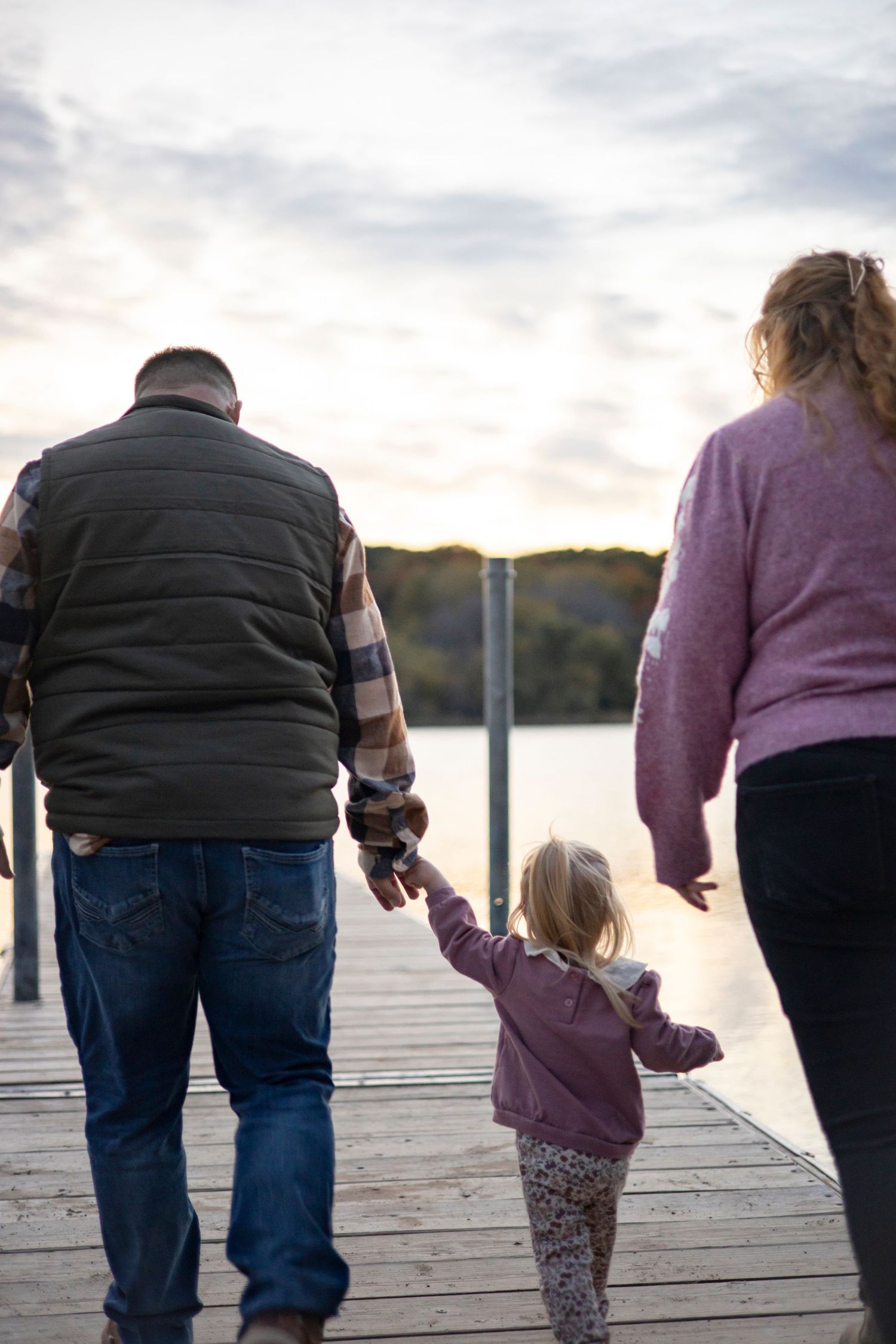Family holding hands while walking on a wooden dock by the lake.