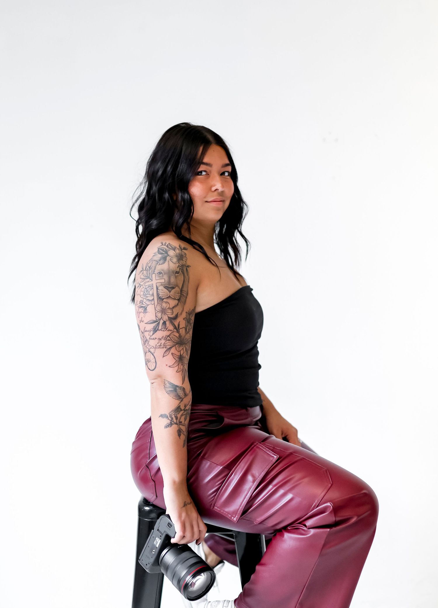 Model in black top and burgundy leather pants poses with camera in stylized photo series.