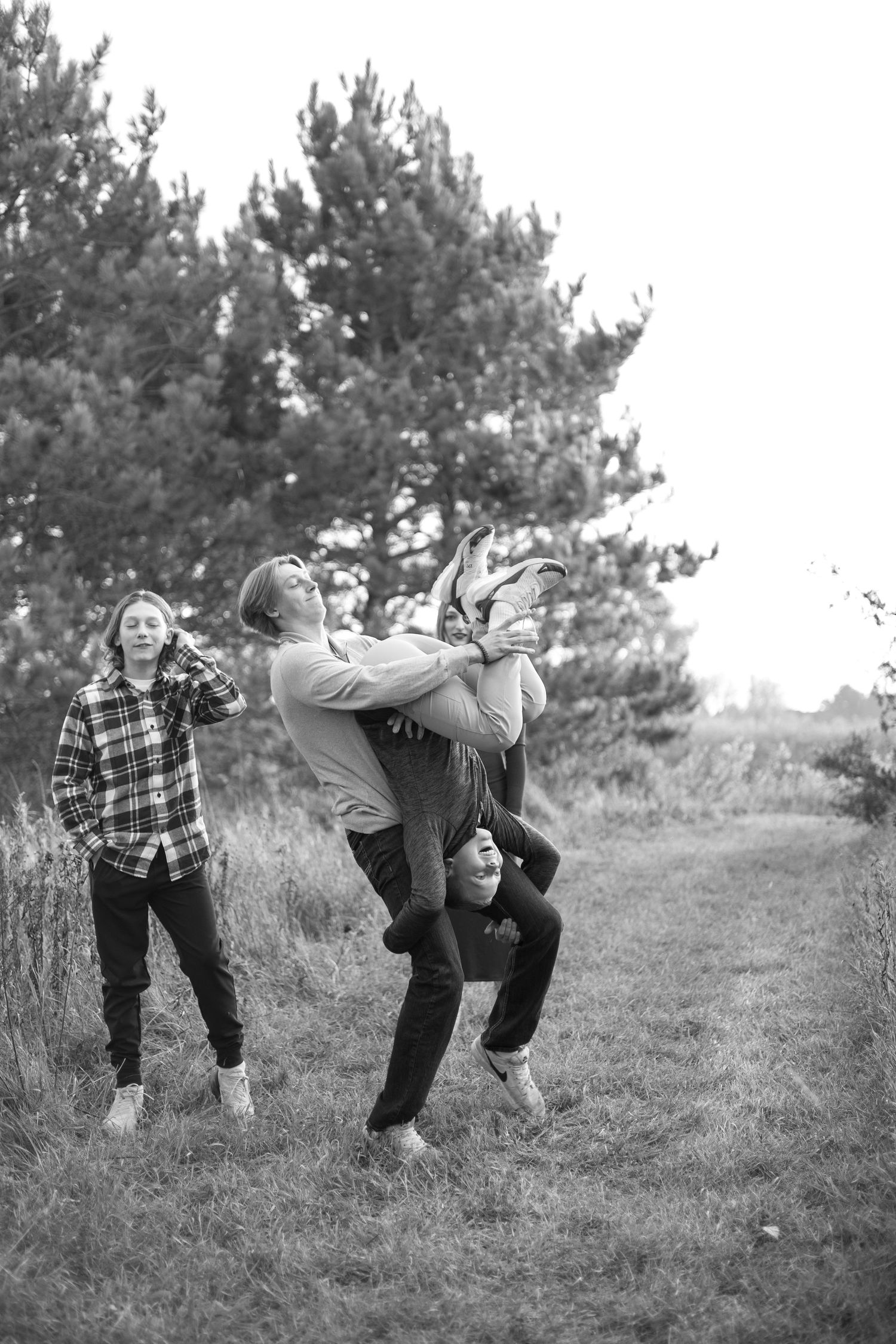 Group plays and jumps playfully in black and white photo on grassy hillside.