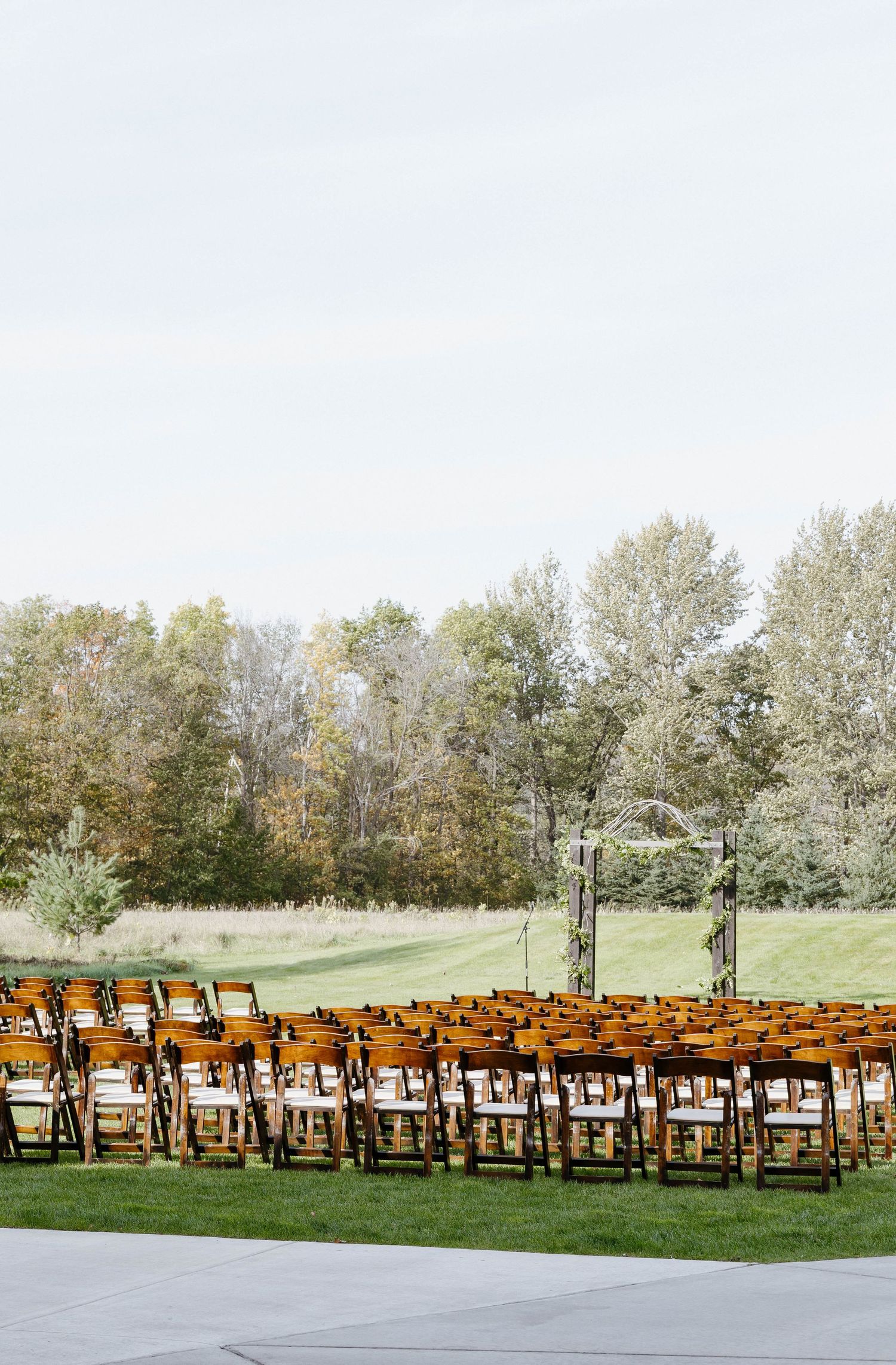 Rows of wooden chairs set up for outdoor wedding ceremony with trees in background.